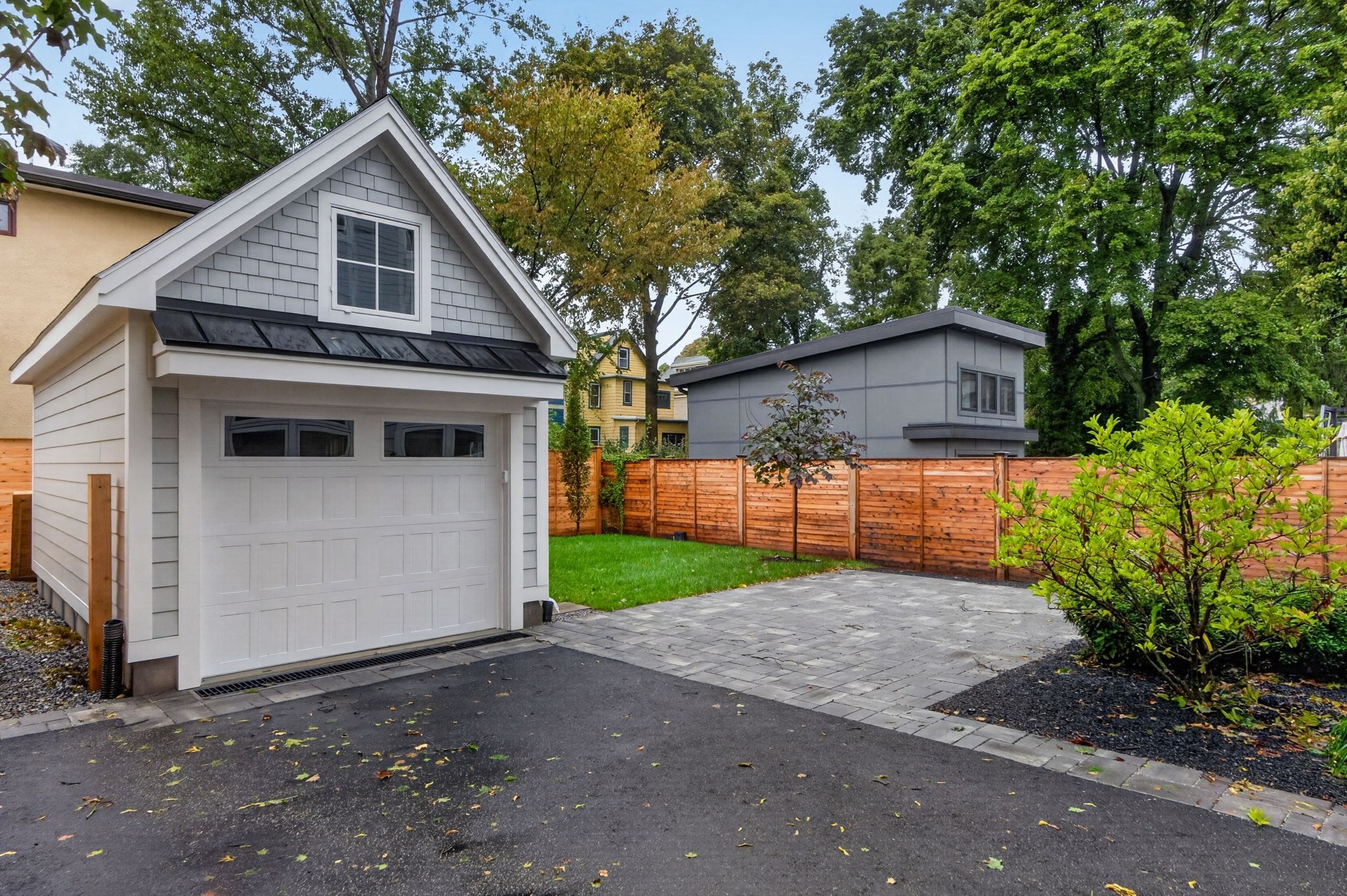 Gray detached garage with a gabled window beside a paved driveway and fenced yard.