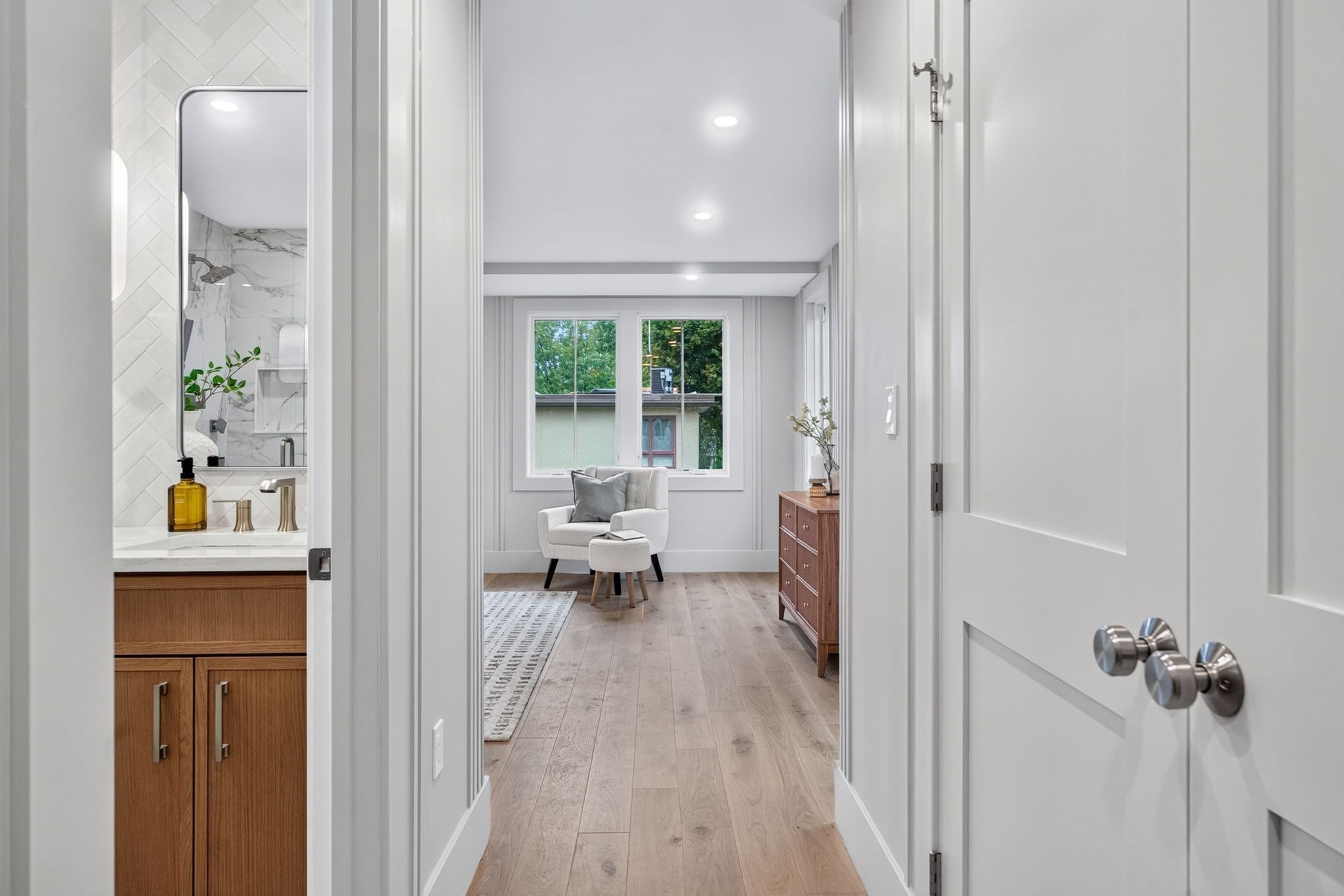 Hallway leading to a sitting area, with a wood vanity visible through the doorway.