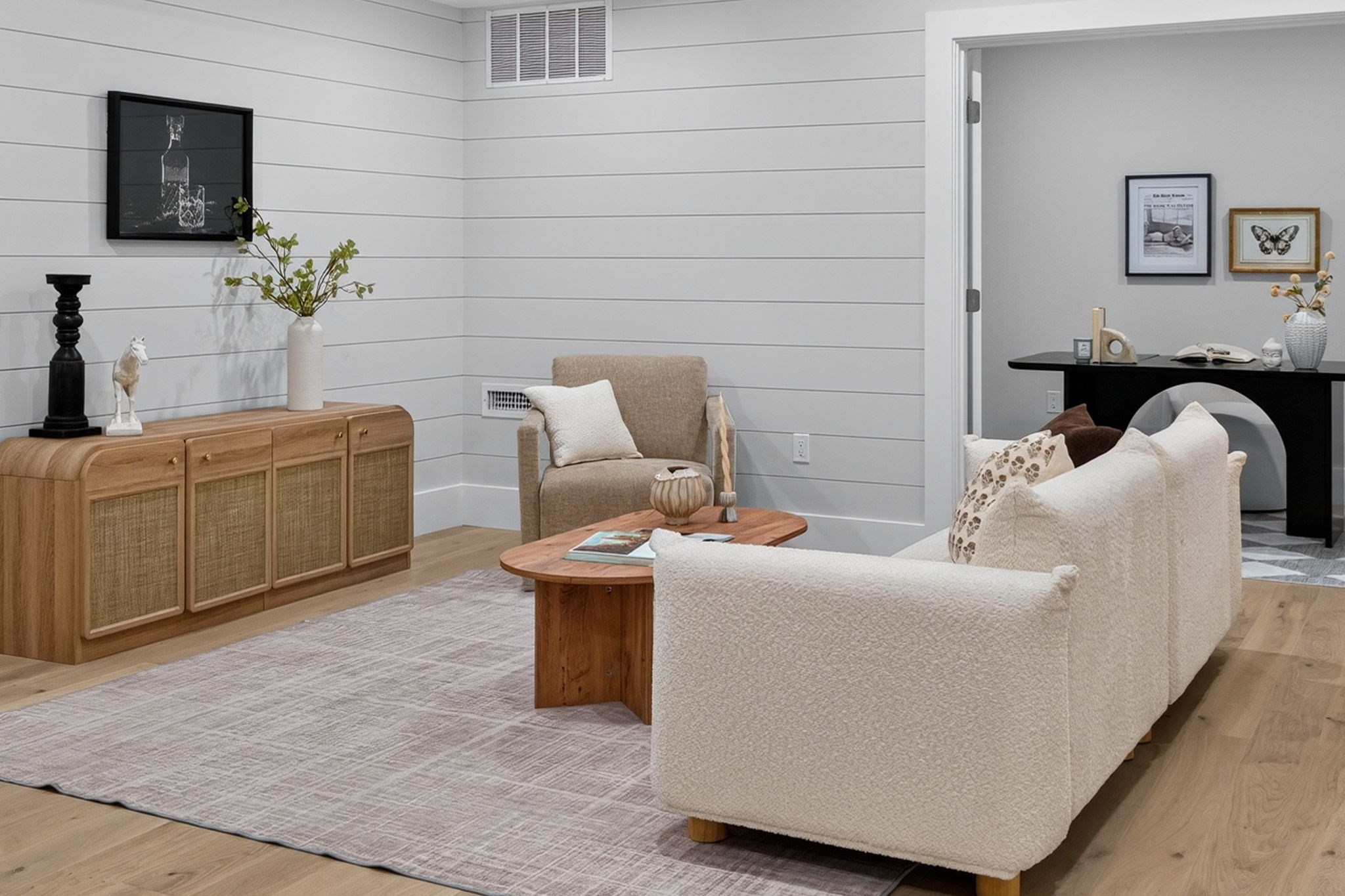 Staged living room with a cream sofa, wood coffee table, and woven-front sideboard against white shiplap walls.
