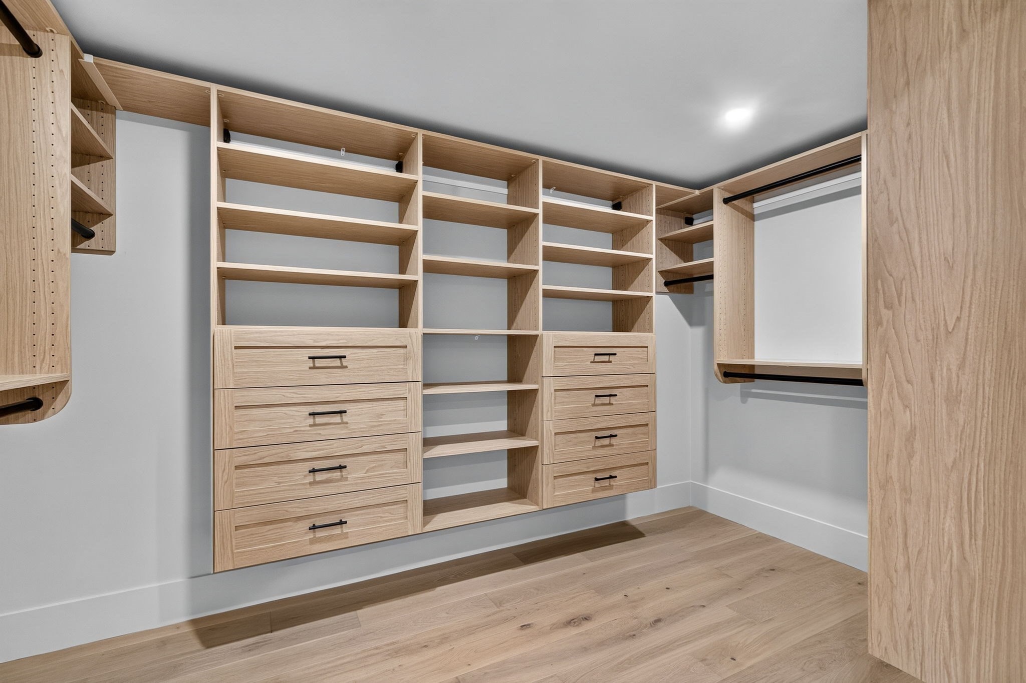 Walk-in closet with custom light-wood shelving, multiple drawers, and hanging rods.