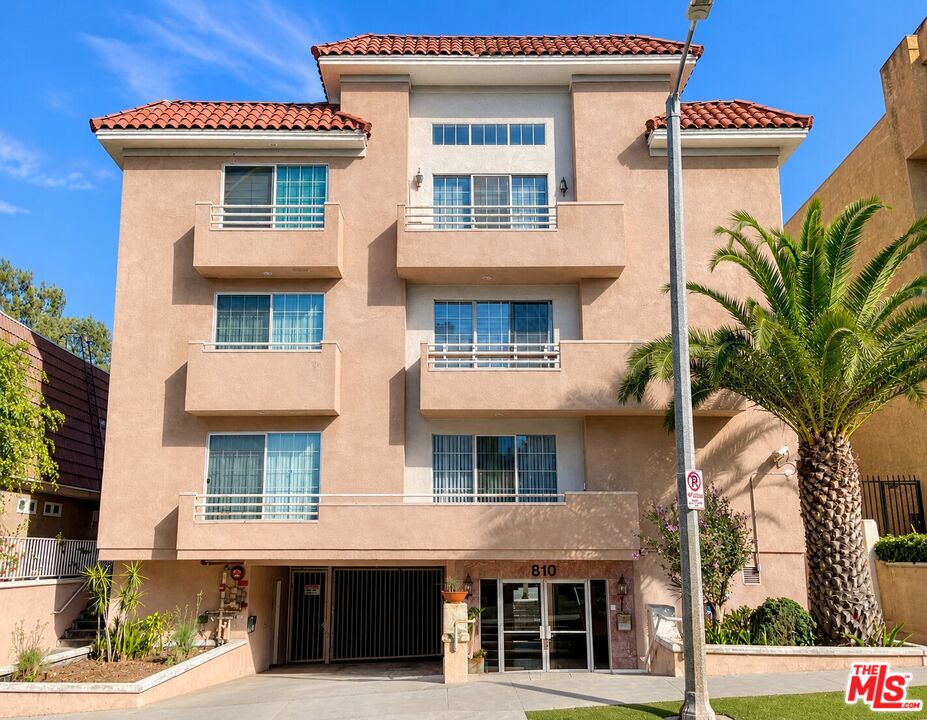 Multi-story peach stucco apartment building with red tile roofs, balconies, and a palm tree.