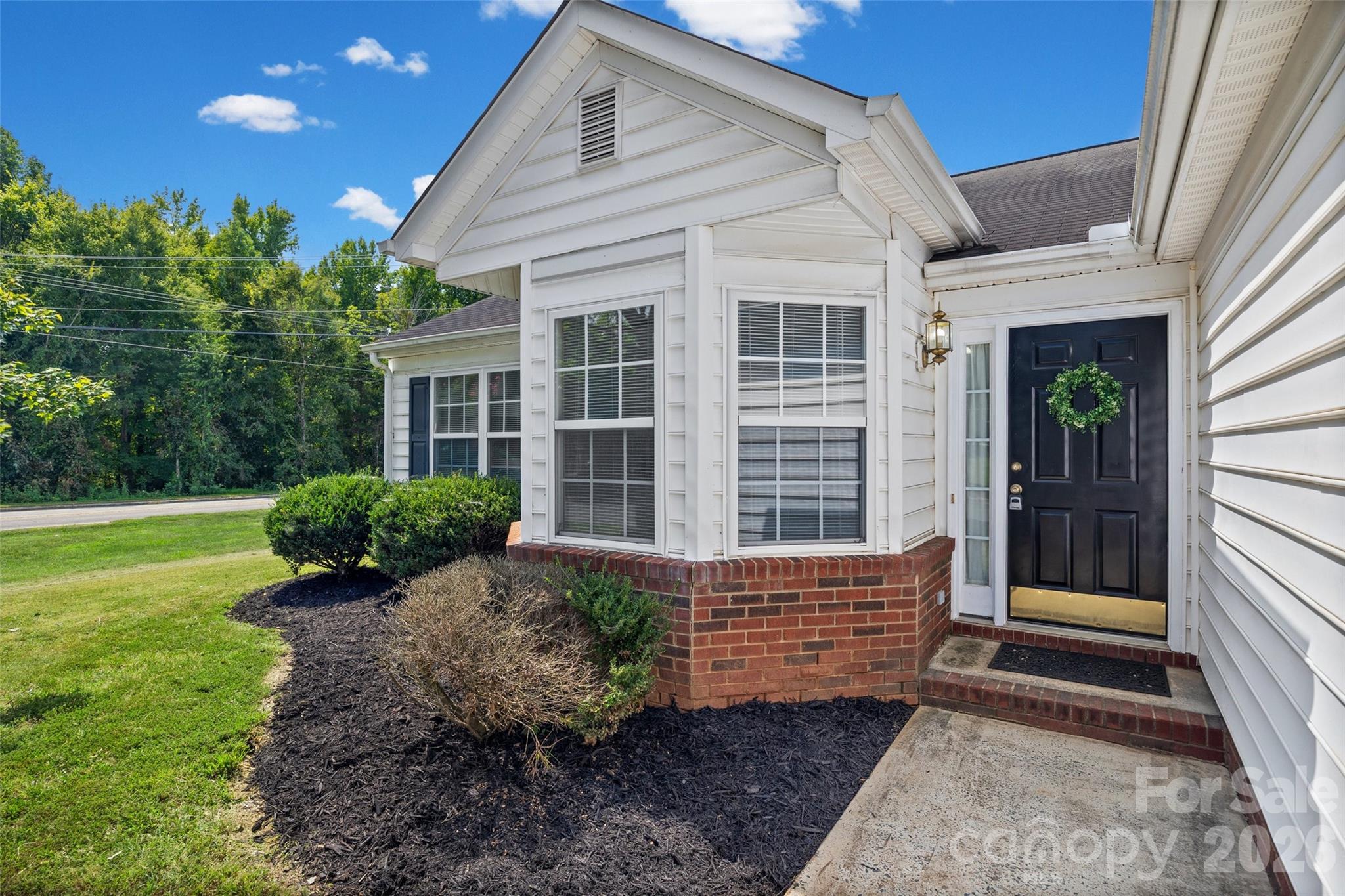 Home entrance with black door and wreath, bay windows, brick base, and landscaped walkway.
