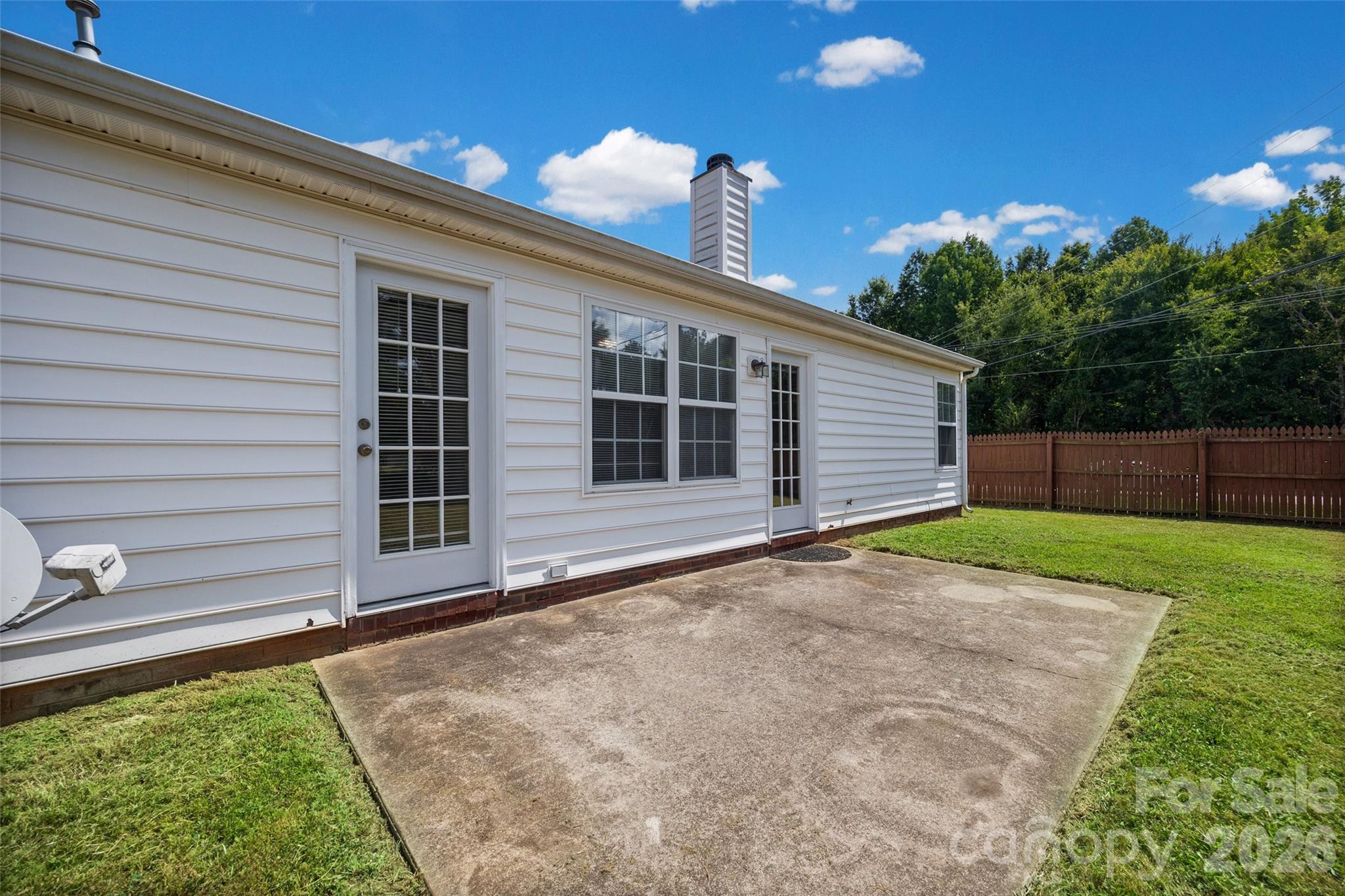 House backyard with a broad concrete patio, glass doors, and a fenced lawn.