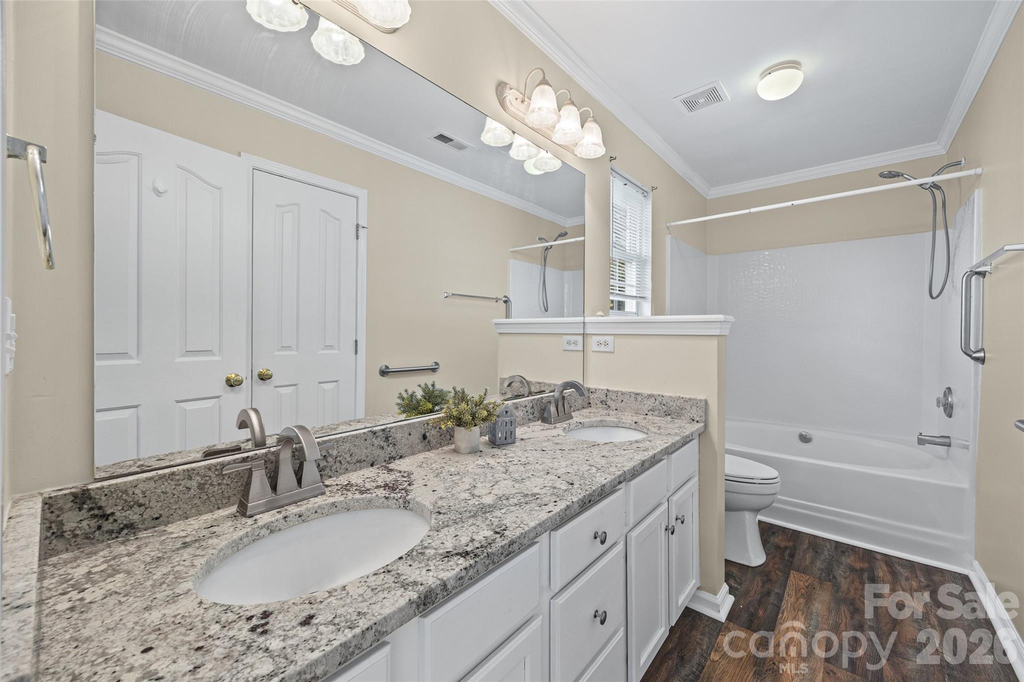 Bathroom with a granite double vanity, large mirror, and white tub-shower combination.