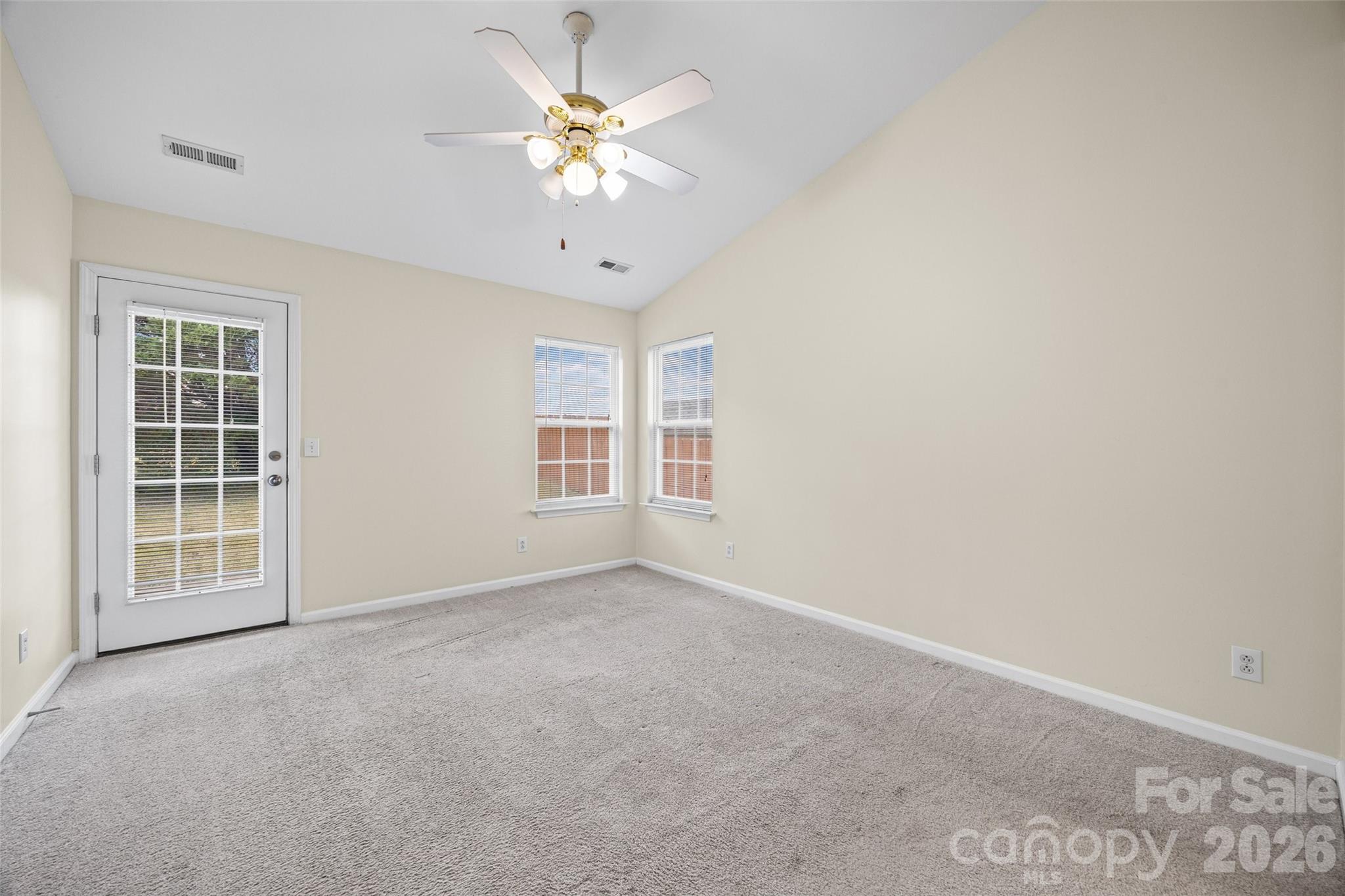 Vacant carpeted room with a ceiling fan, two windows, and a glass-paneled exterior door.