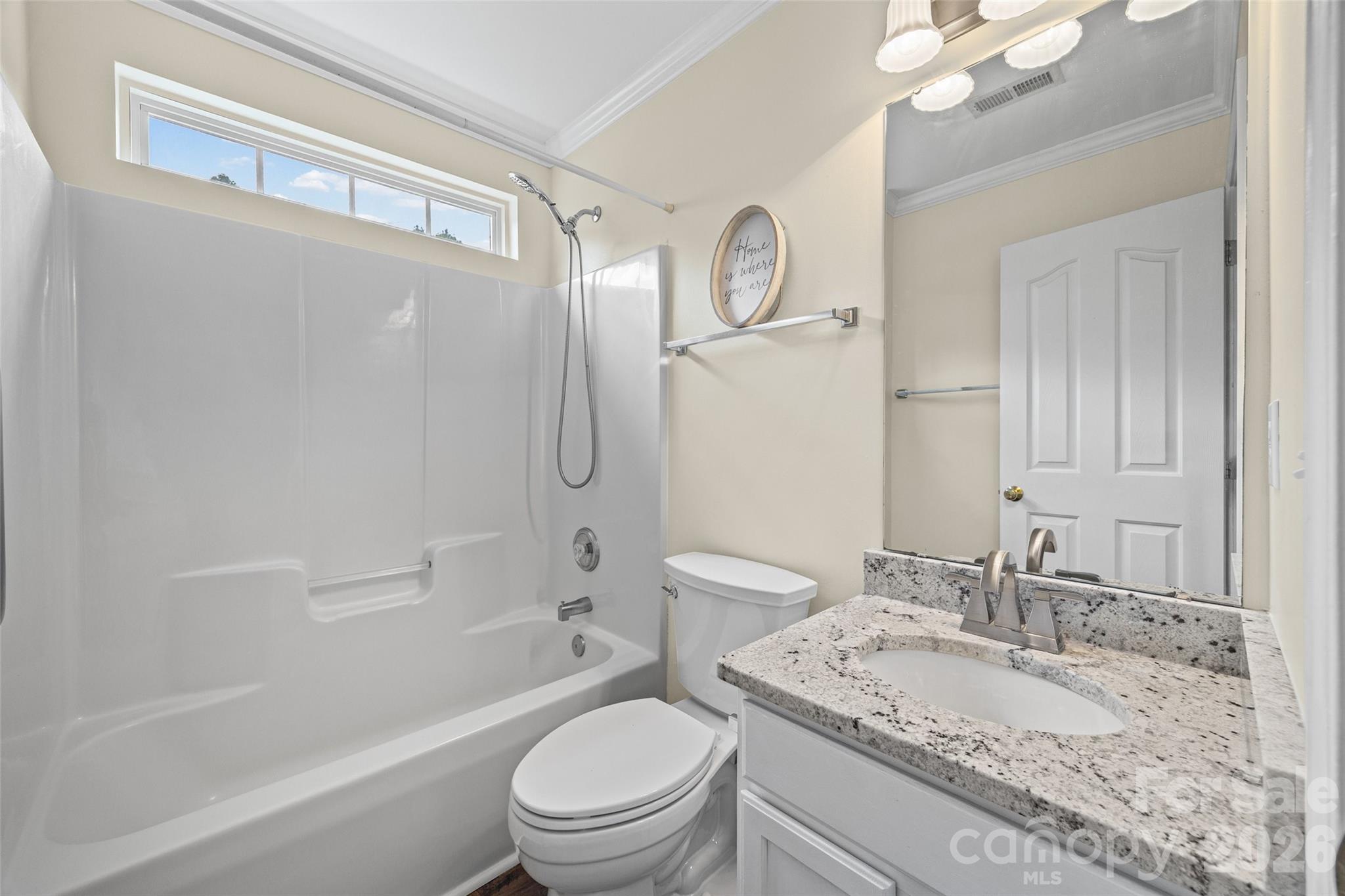 Bathroom with a white tub and shower, high window, and granite-topped vanity.