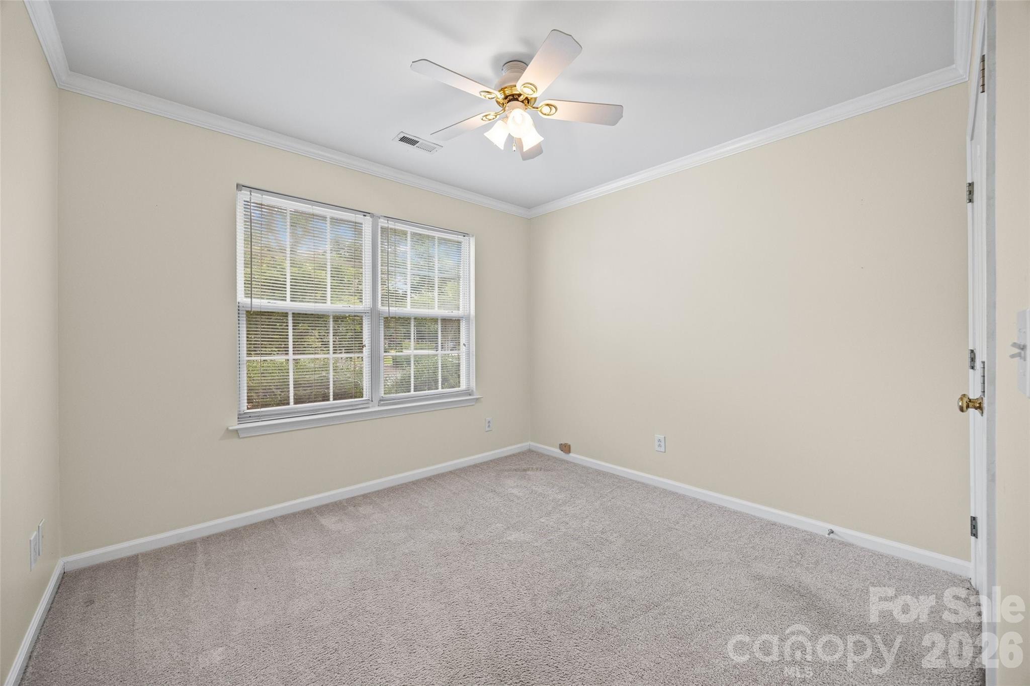 Empty carpeted bedroom with two blind-covered windows and a ceiling fan with lights.