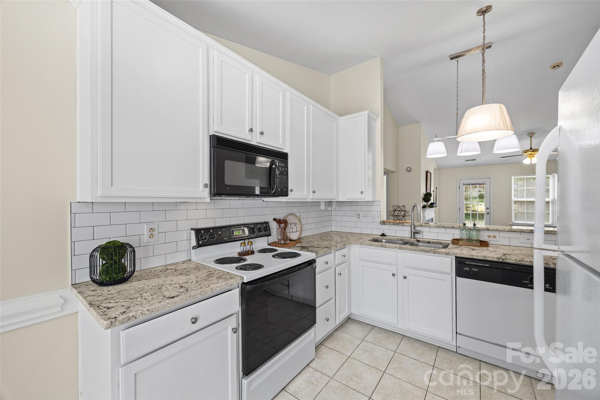 Bright kitchen with white cabinets, speckled stone counters, subway tile backsplash, and stainless-steel appliances.