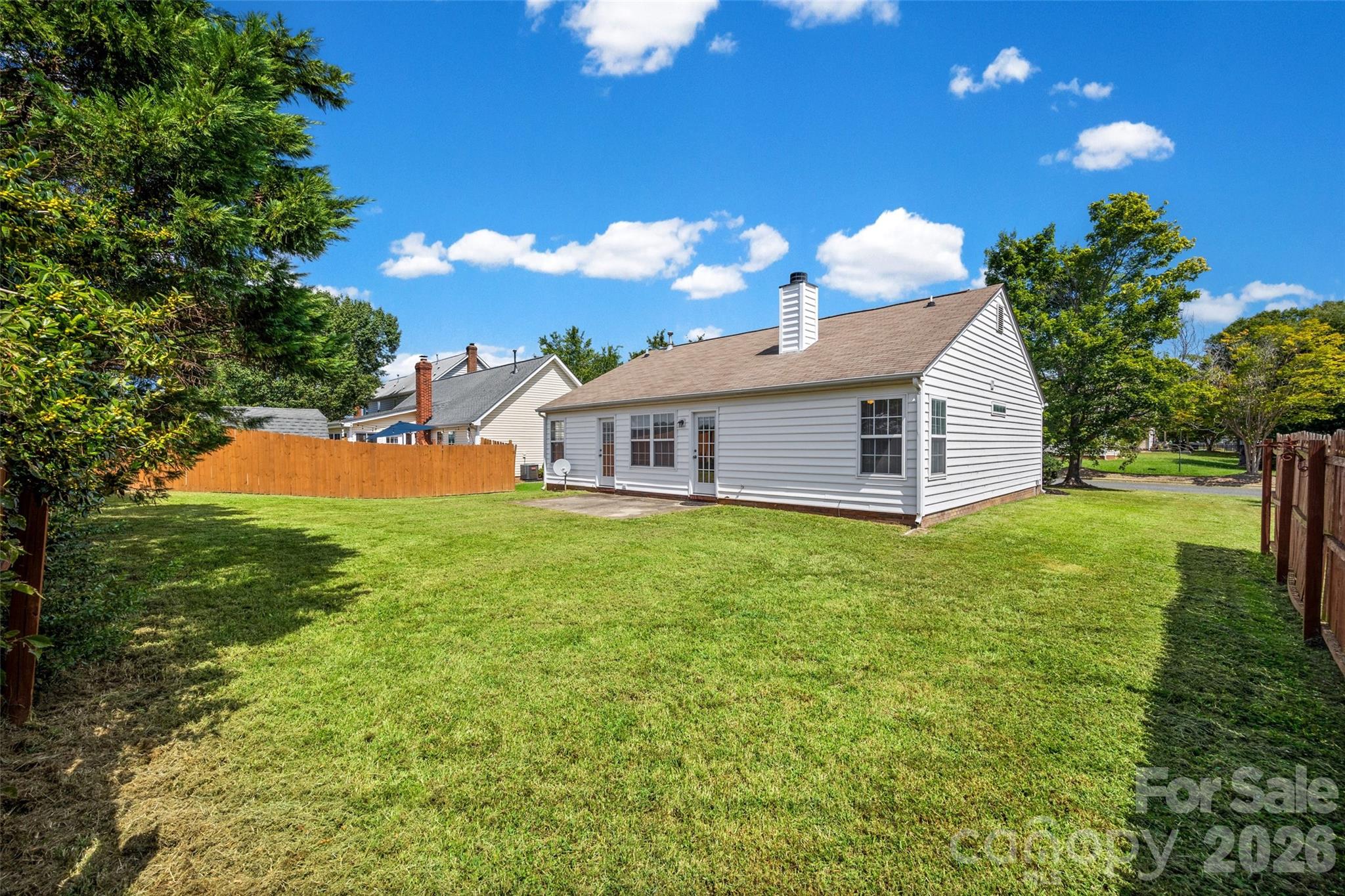 White-sided house and fenced backyard with a broad lawn and mature trees.