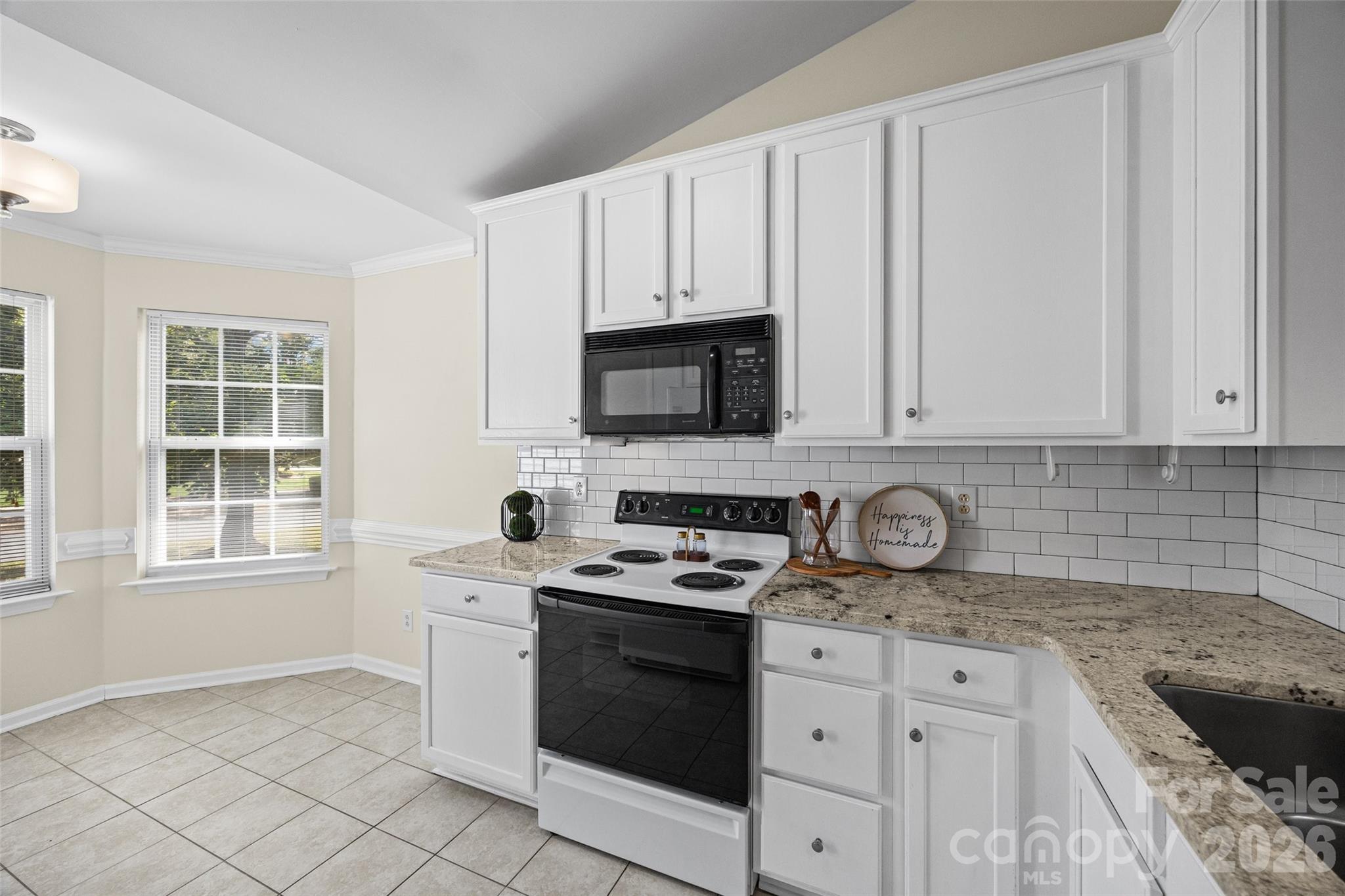Kitchen with white cabinets, granite counters, subway tile backsplash, and a black microwave above the range.