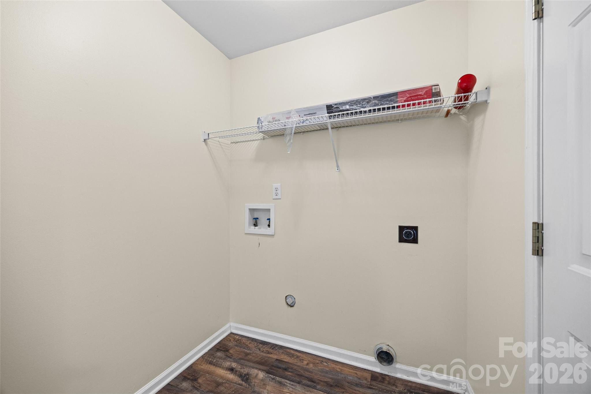 Empty laundry room with washer hookups, dryer vent, and a wire storage shelf.
