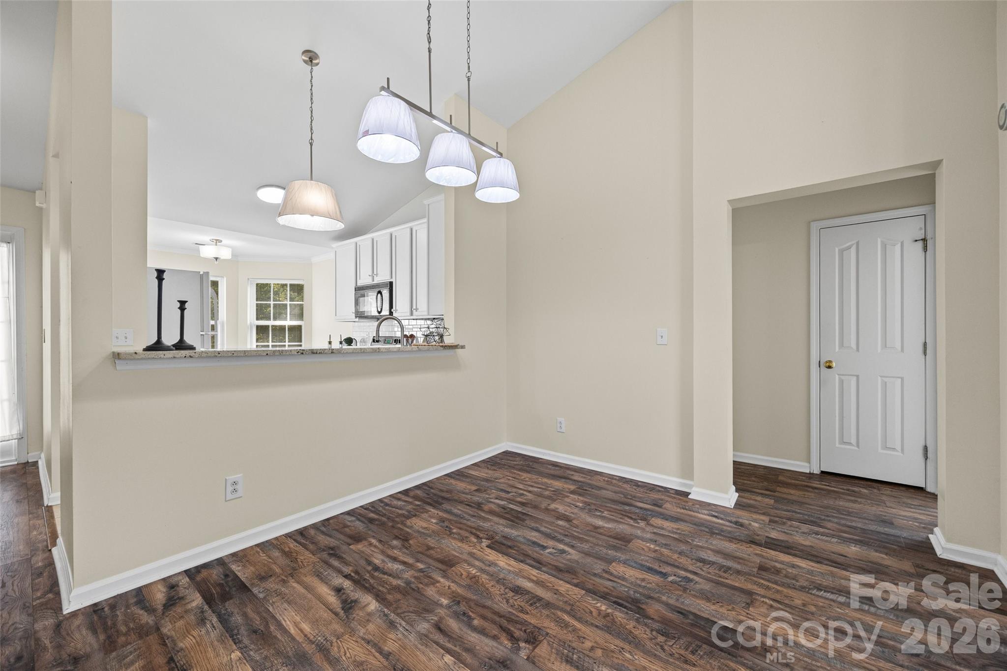 Open dining area with dark wood flooring, a breakfast bar, white kitchen cabinets, and hanging pendant lights.