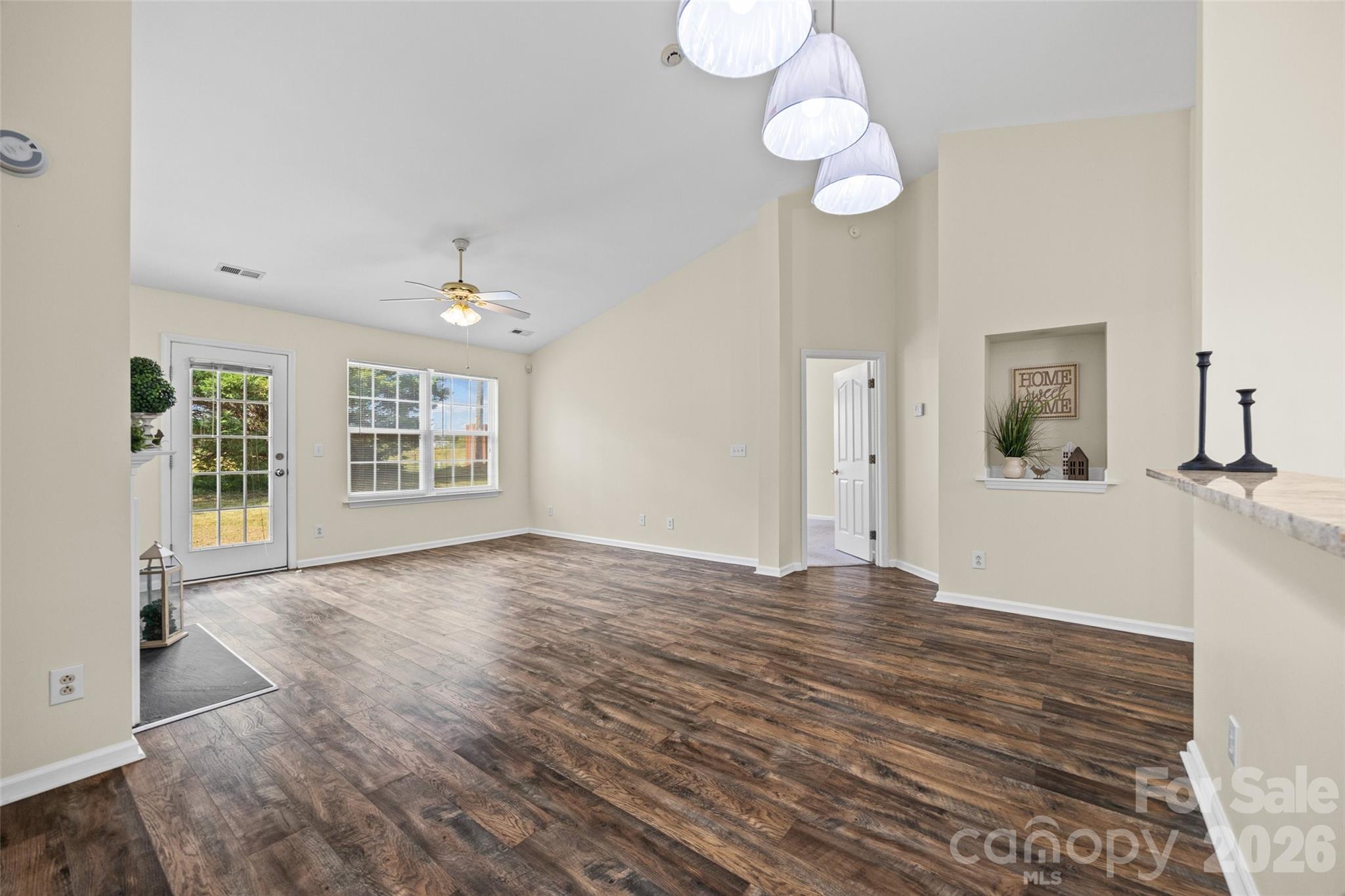 Open living area with dark wood-look floors, vaulted ceiling, and large windows.