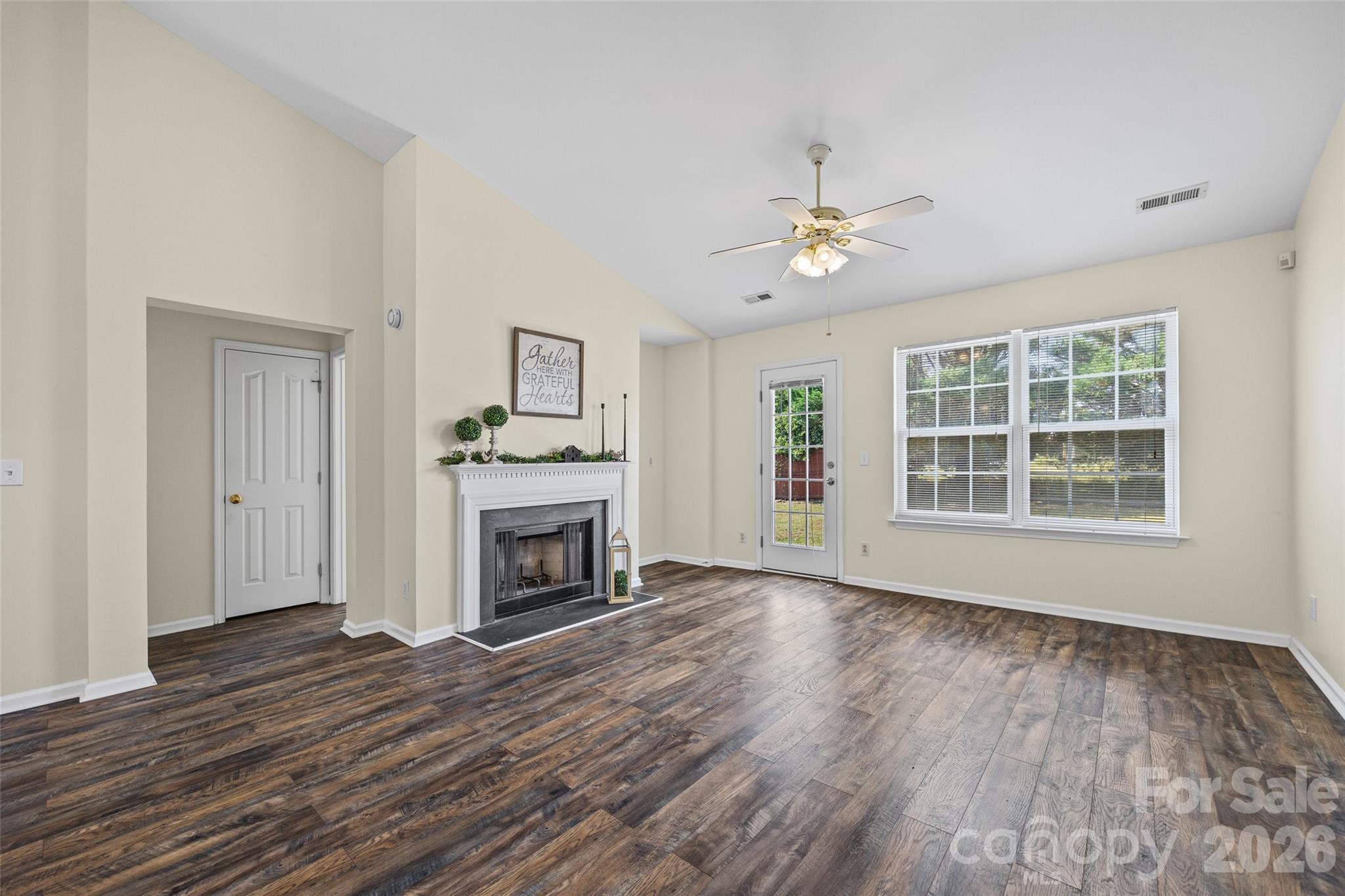 Unfurnished living room with dark wood-look floors, a white fireplace, ceiling fan, and large windows.