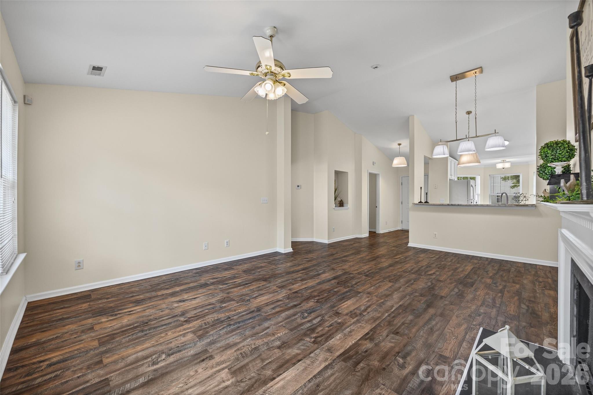 Open-plan living and dining area with dark wood-look floors, ceiling fan, kitchen counter, and fireplace.