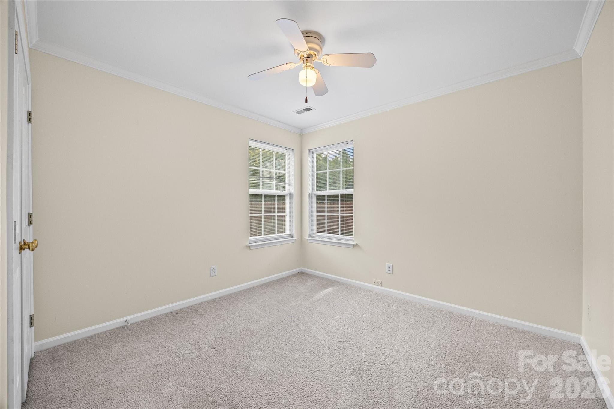 Empty carpeted bedroom with two corner windows and a ceiling fan with a light.