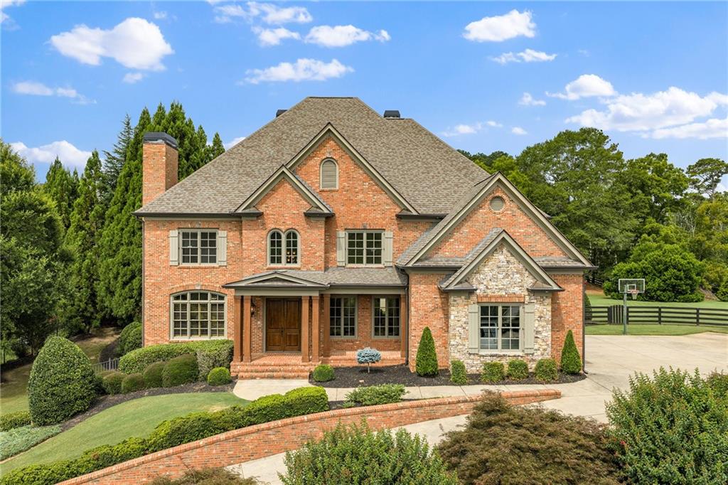 Two-story brick and stone house with landscaped grounds and a basketball hoop beside the driveway.