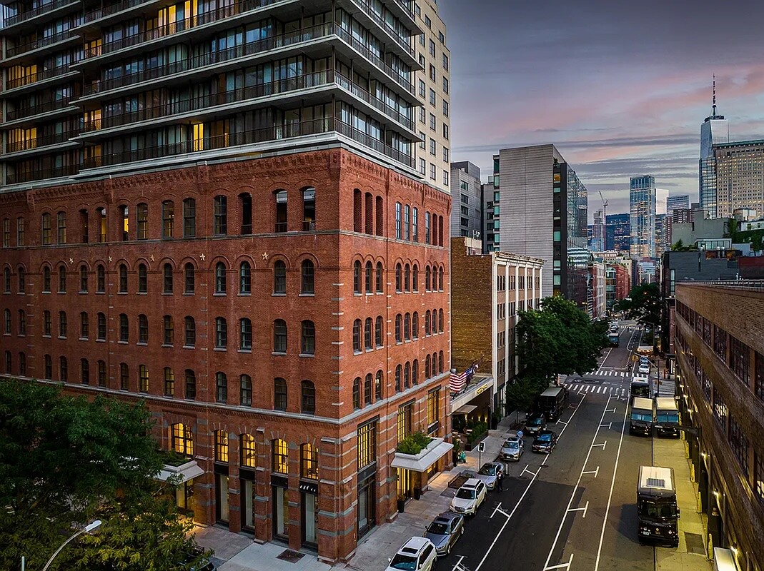100 Vandam Street’s red-brick façade and modern tower overlook a downtown street at dusk.