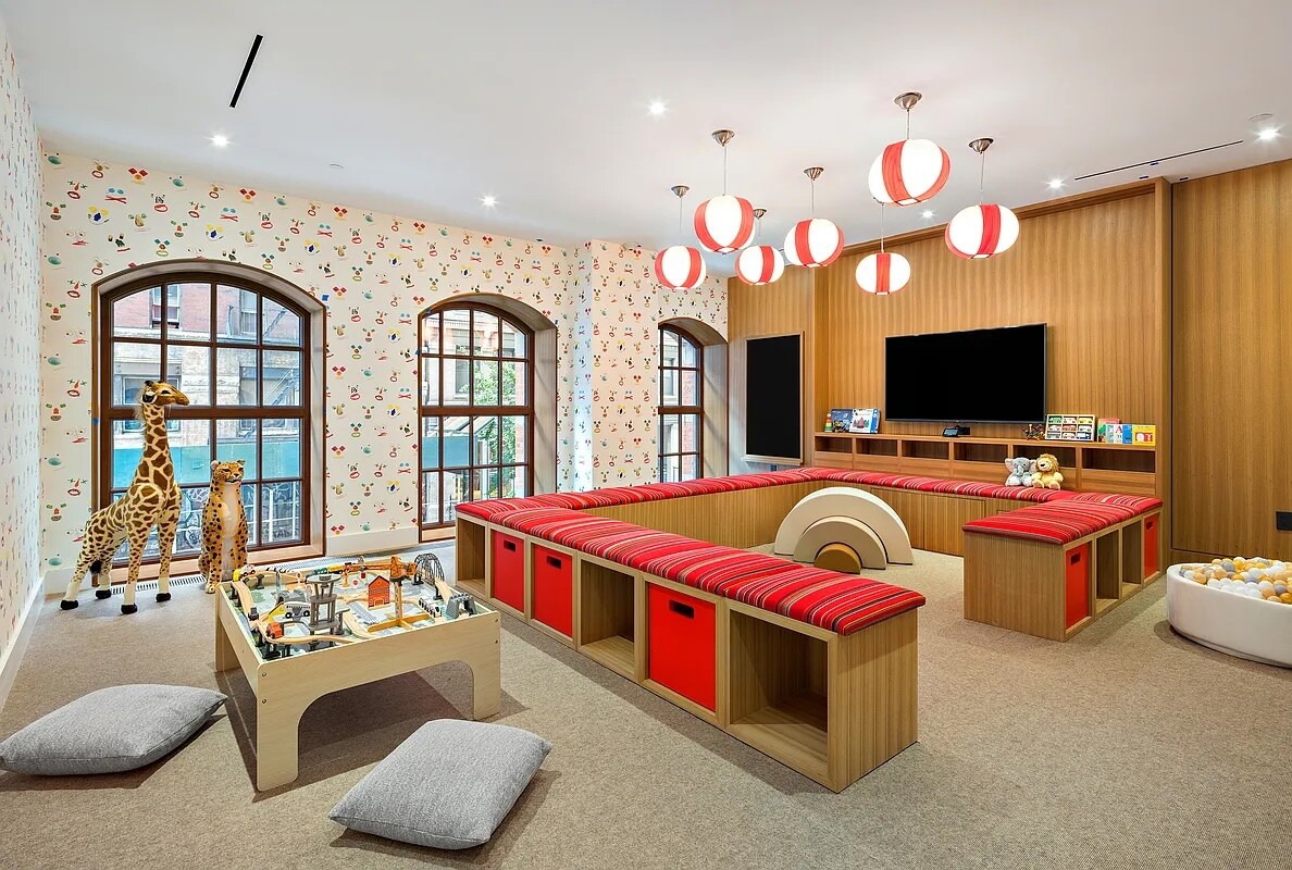 Children’s playroom with a toy train table, animal figures, red-striped benches, and arched windows.