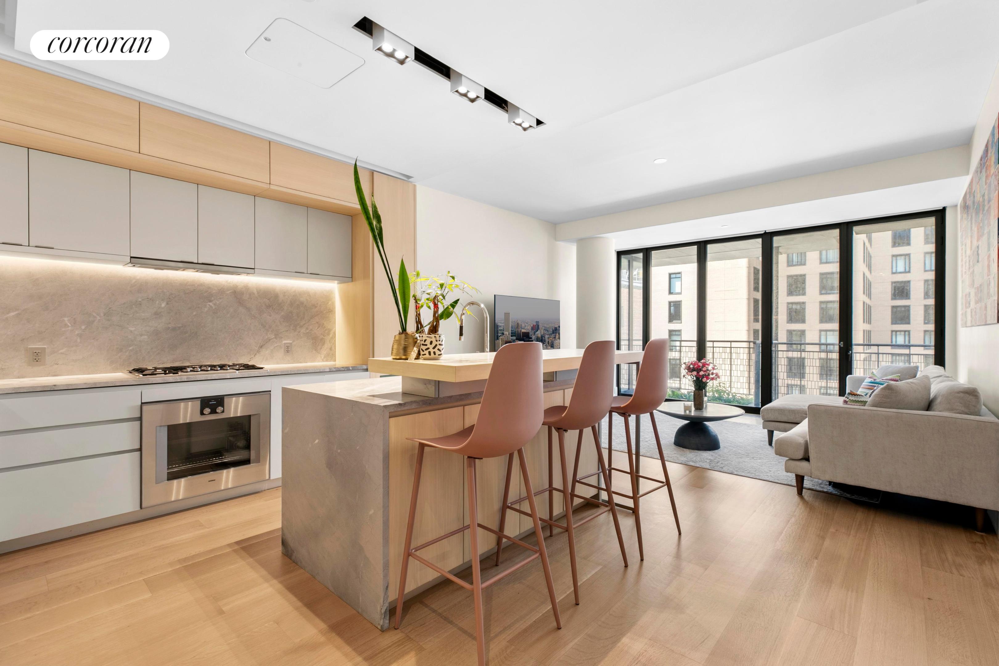 Open-plan kitchen with a stone island and bar stools beside floor-to-ceiling windows.