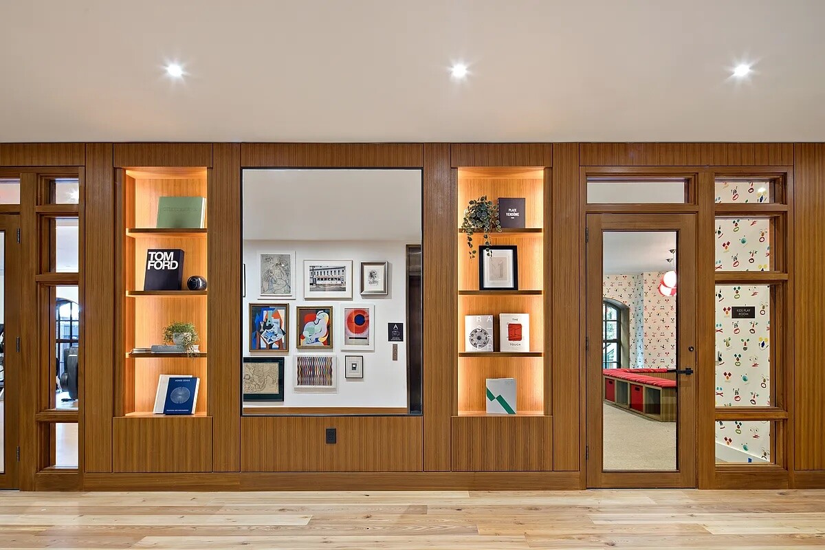 Walnut built-in cabinetry with illuminated shelves and glass doors opening to a children’s playroom.