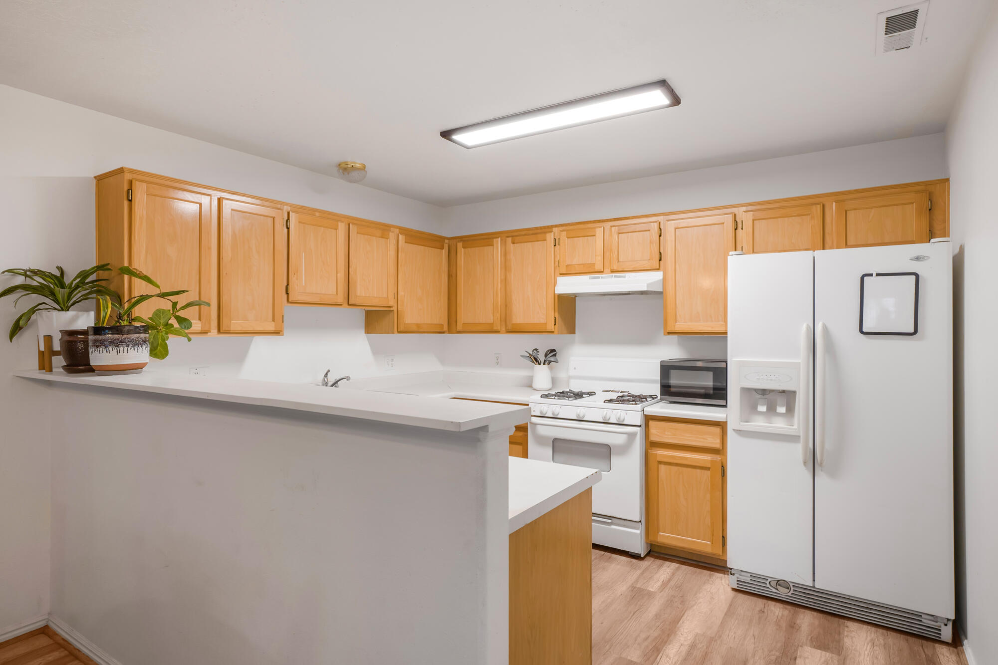 Kitchen with honey-colored cabinets, white countertops, peninsula, and white appliances.