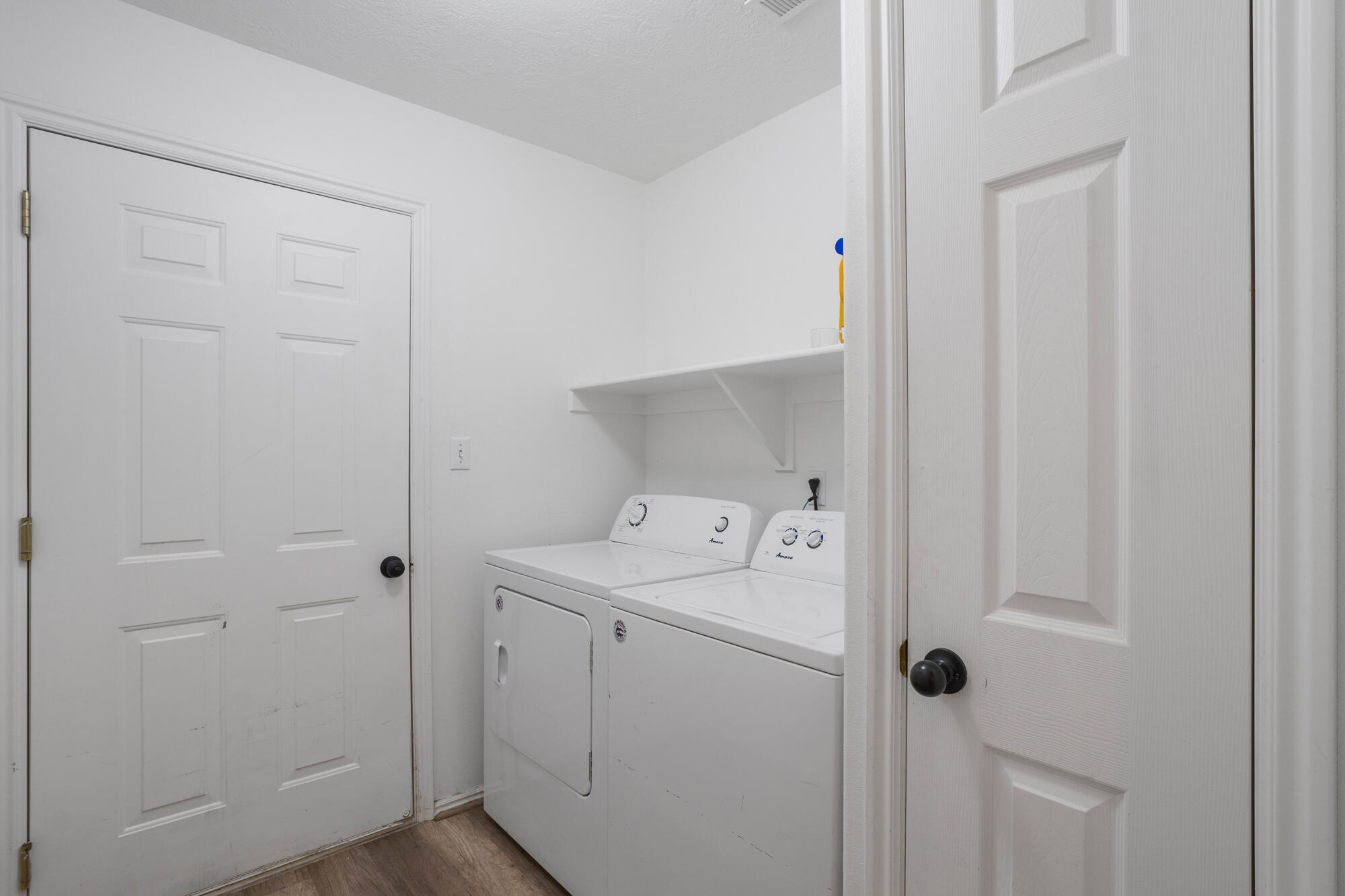 Laundry room with white washer and dryer beneath a wall shelf.