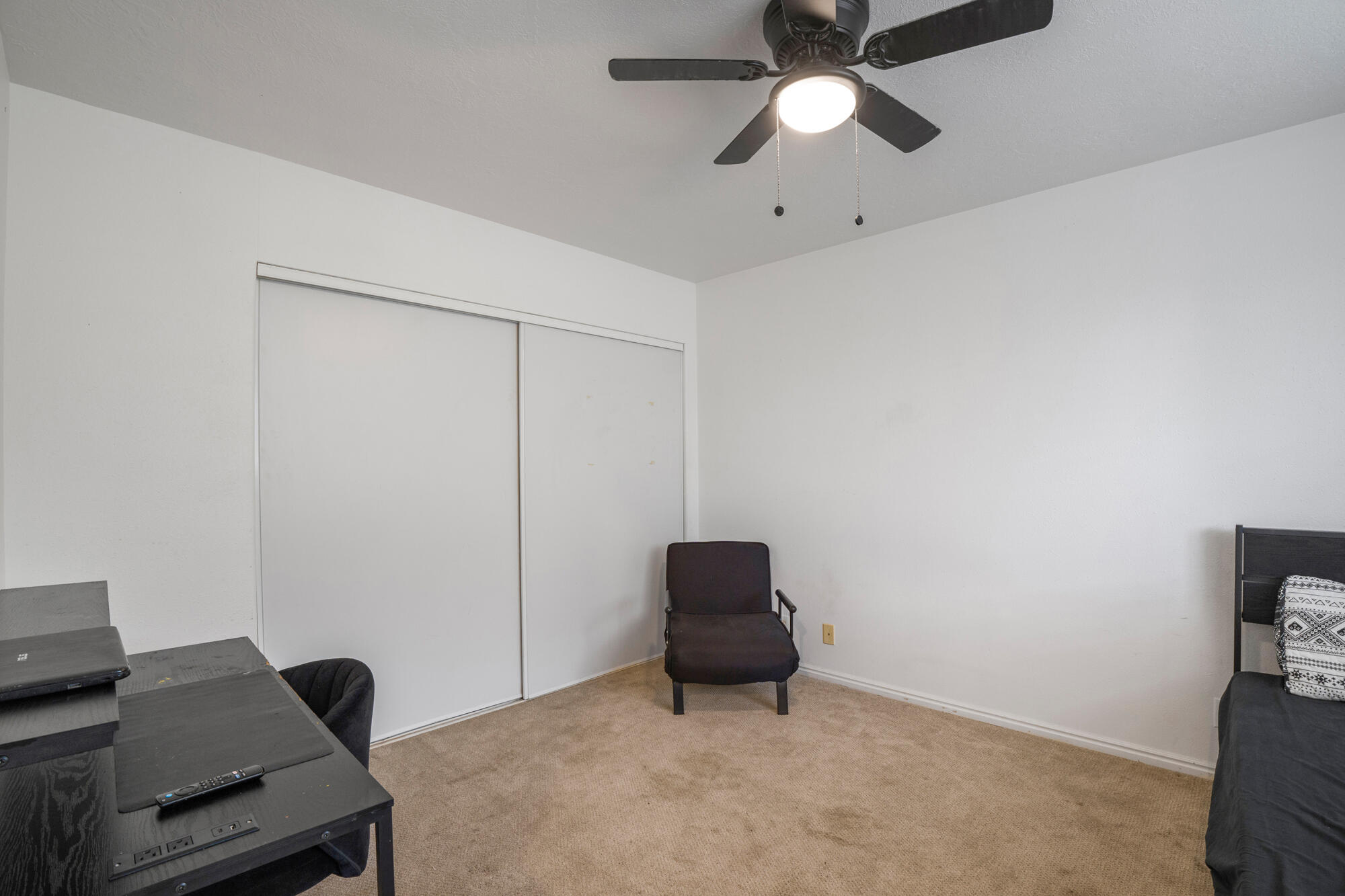 Bedroom with sliding closet doors, beige carpet, a desk, and a ceiling fan.