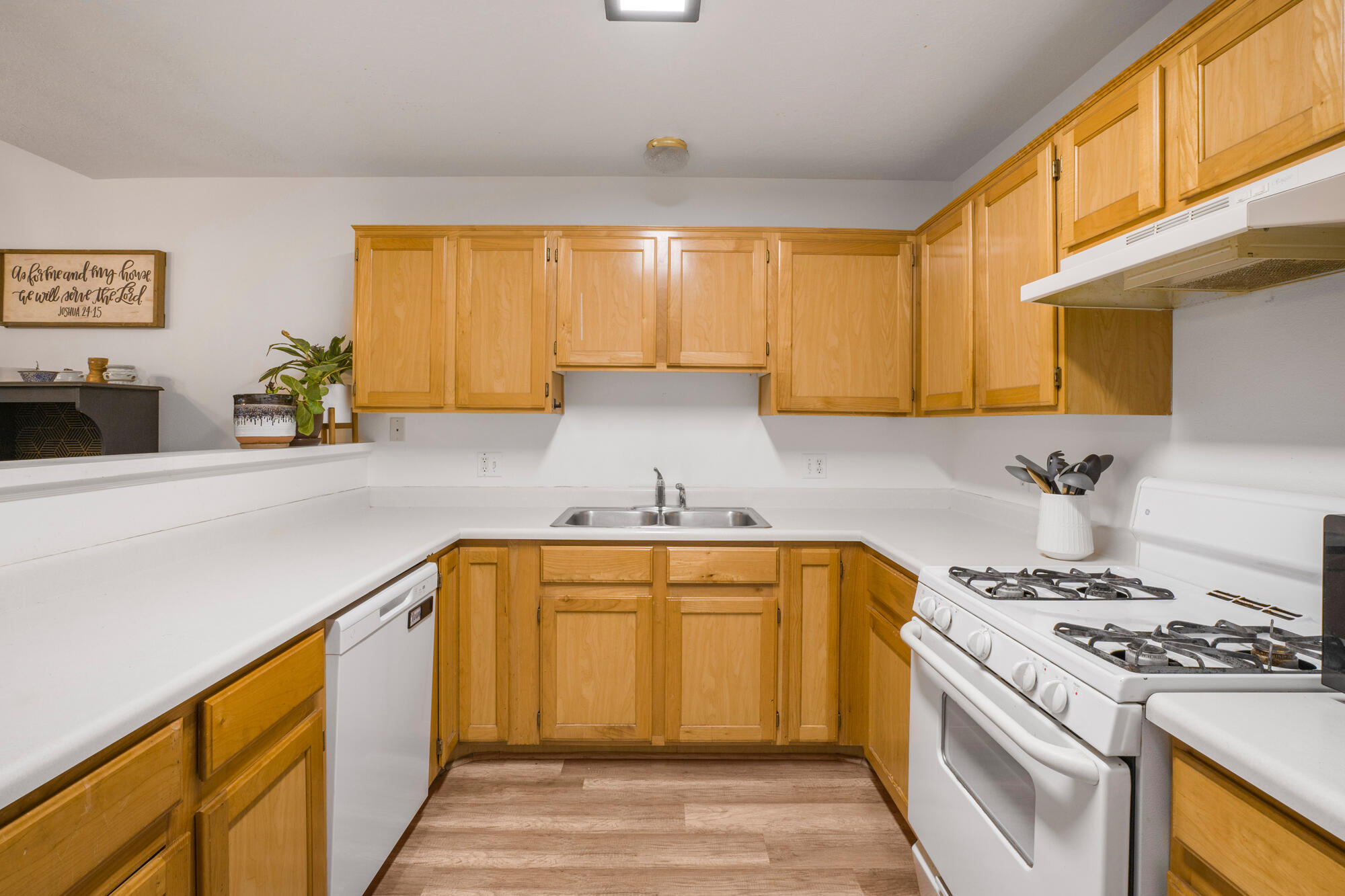 Kitchen with honey-colored wood cabinets, white counters, a double sink, dishwasher, and gas range.