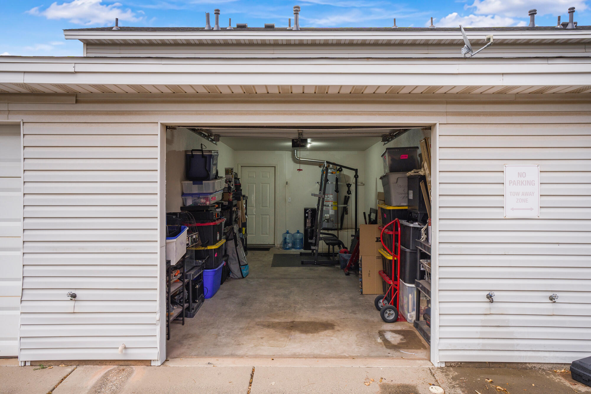 Open garage with storage bins, a weight-training machine, and a red hand truck.