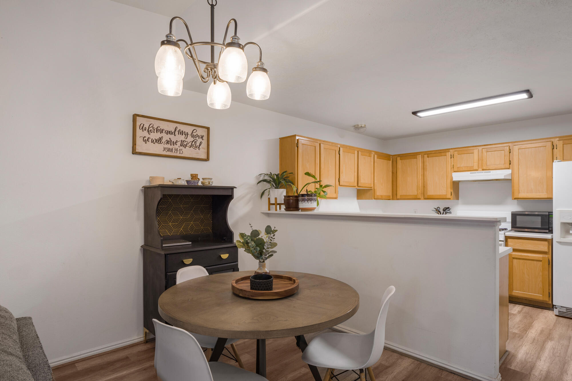 Dining area with a round wooden table beside an open kitchen with light wood cabinets and a breakfast bar.