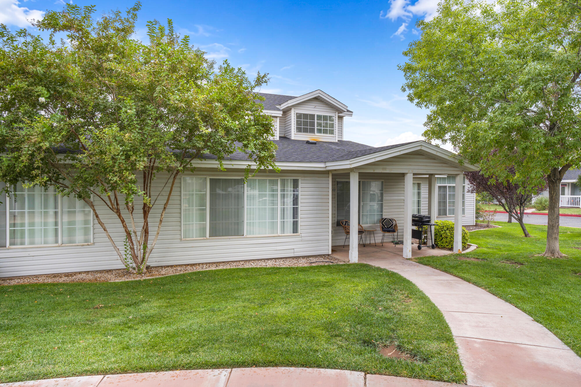 Two-story house with a covered porch, barbecue grill, and curved walkway through a green lawn.