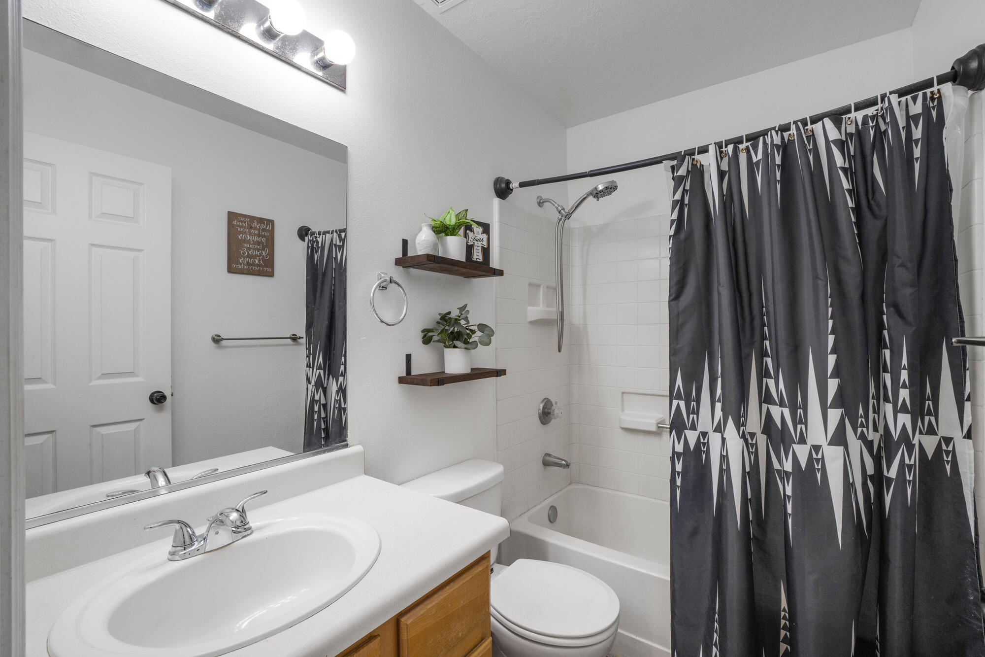 Bathroom with a wood vanity, white tub and tile, and dark geometric shower curtain.