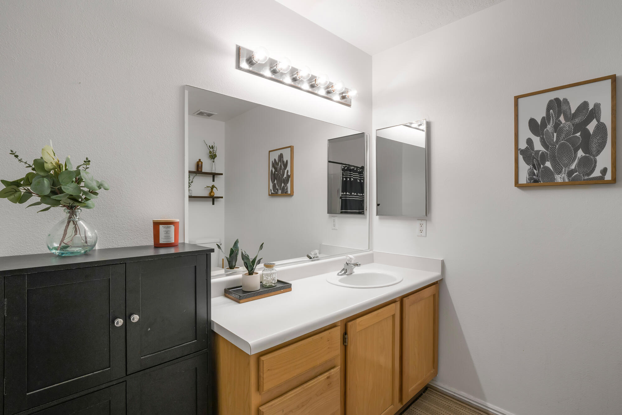 Bathroom vanity with a large mirror, white countertop, light wood cabinets, and a contrasting black storage cabinet.