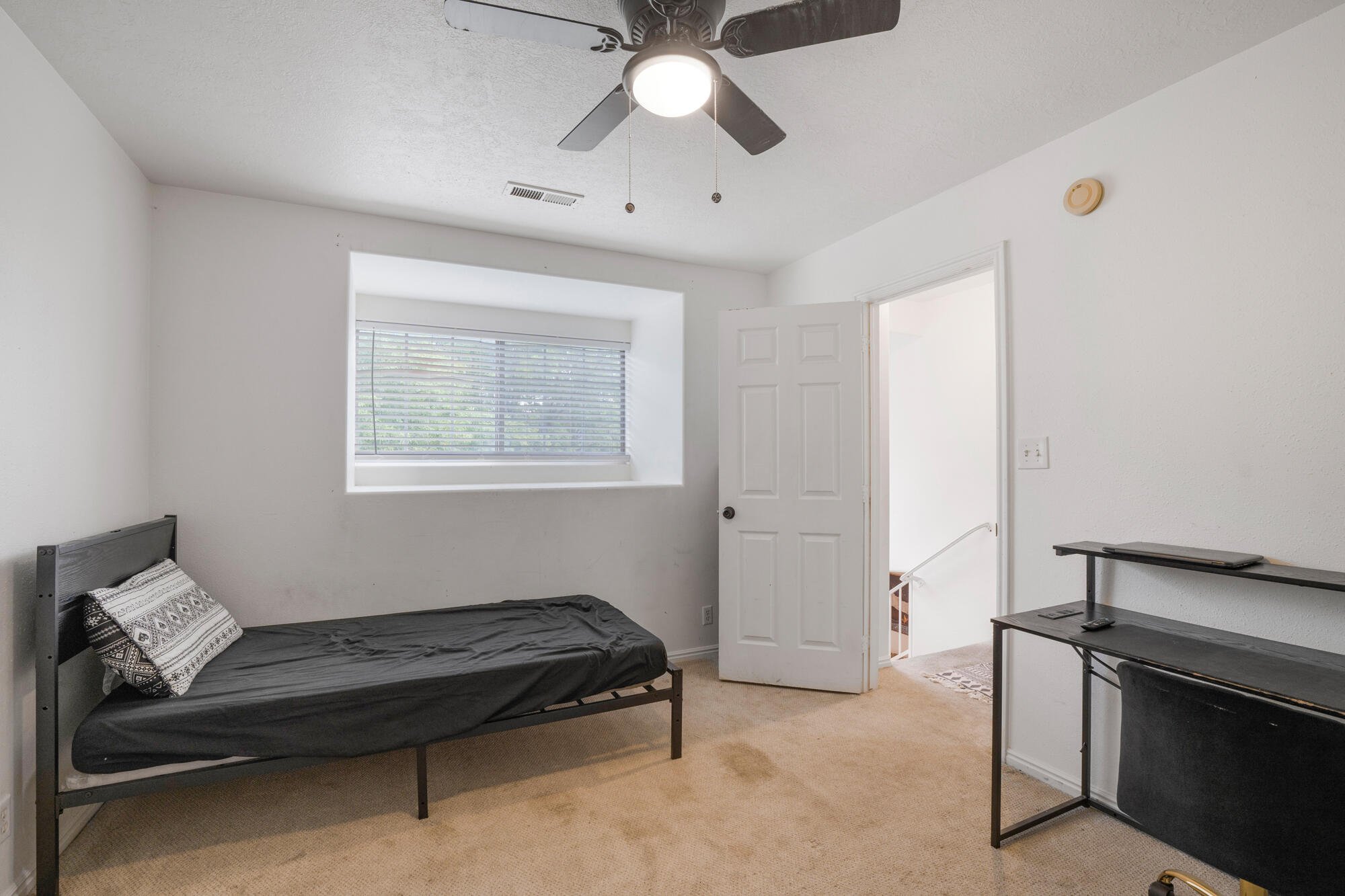 Bedroom with a dark bed, window blinds, and a black desk beside an open door.