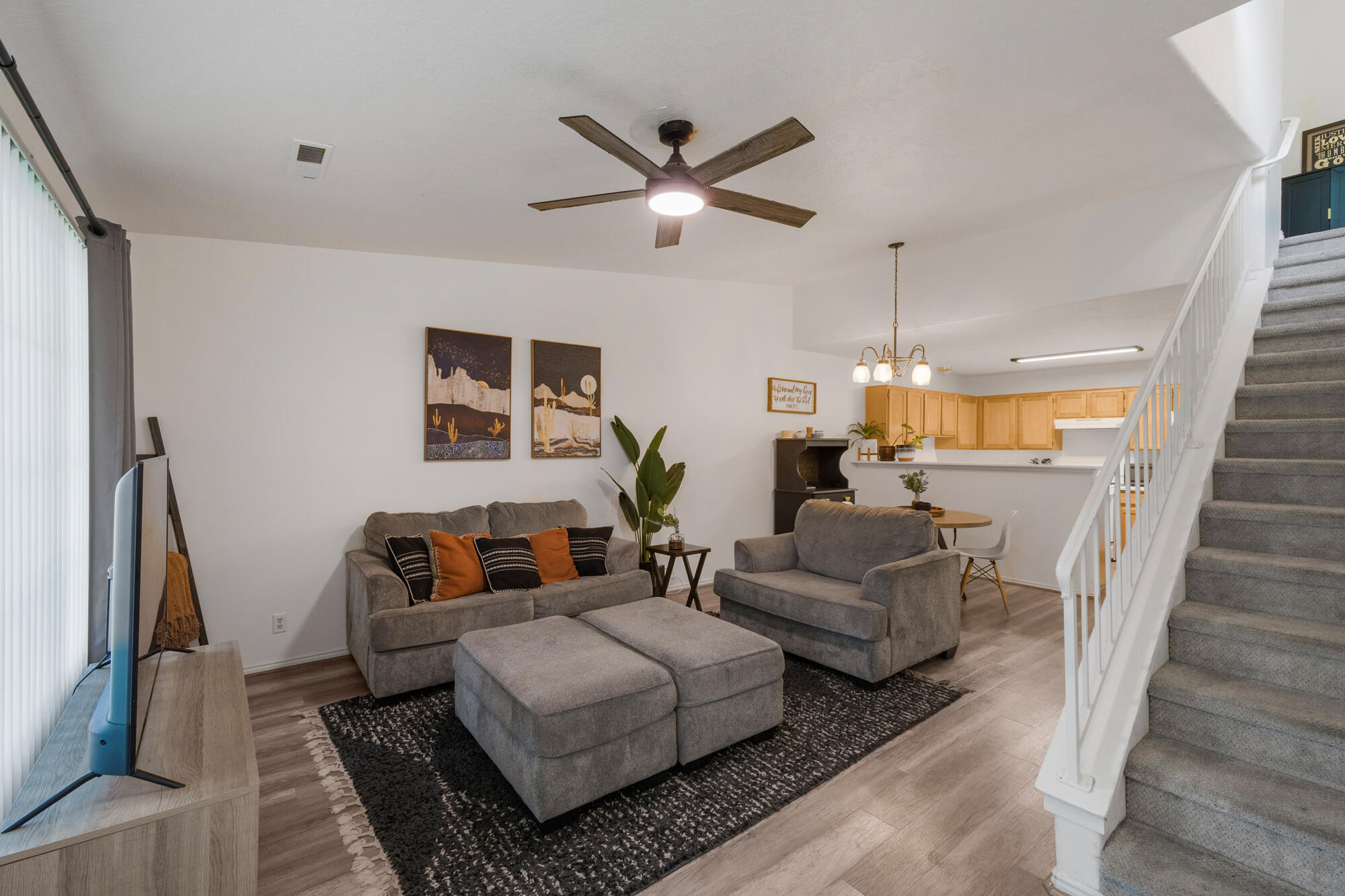 Open-plan living room with gray seating, light wood kitchen cabinets, and carpeted staircase.