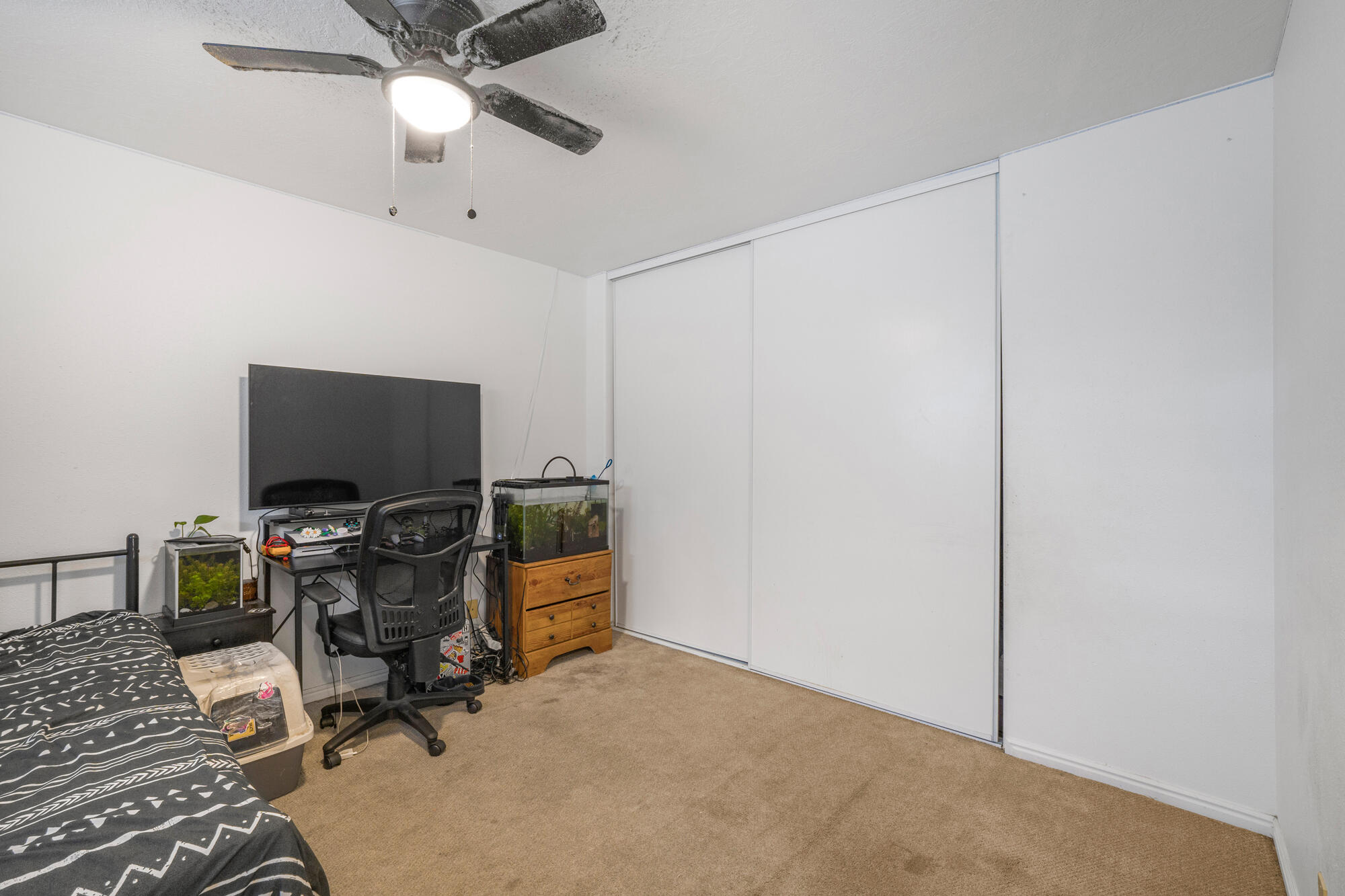 Bedroom with sliding closet doors, a desk, two aquariums, and a patterned bedspread.