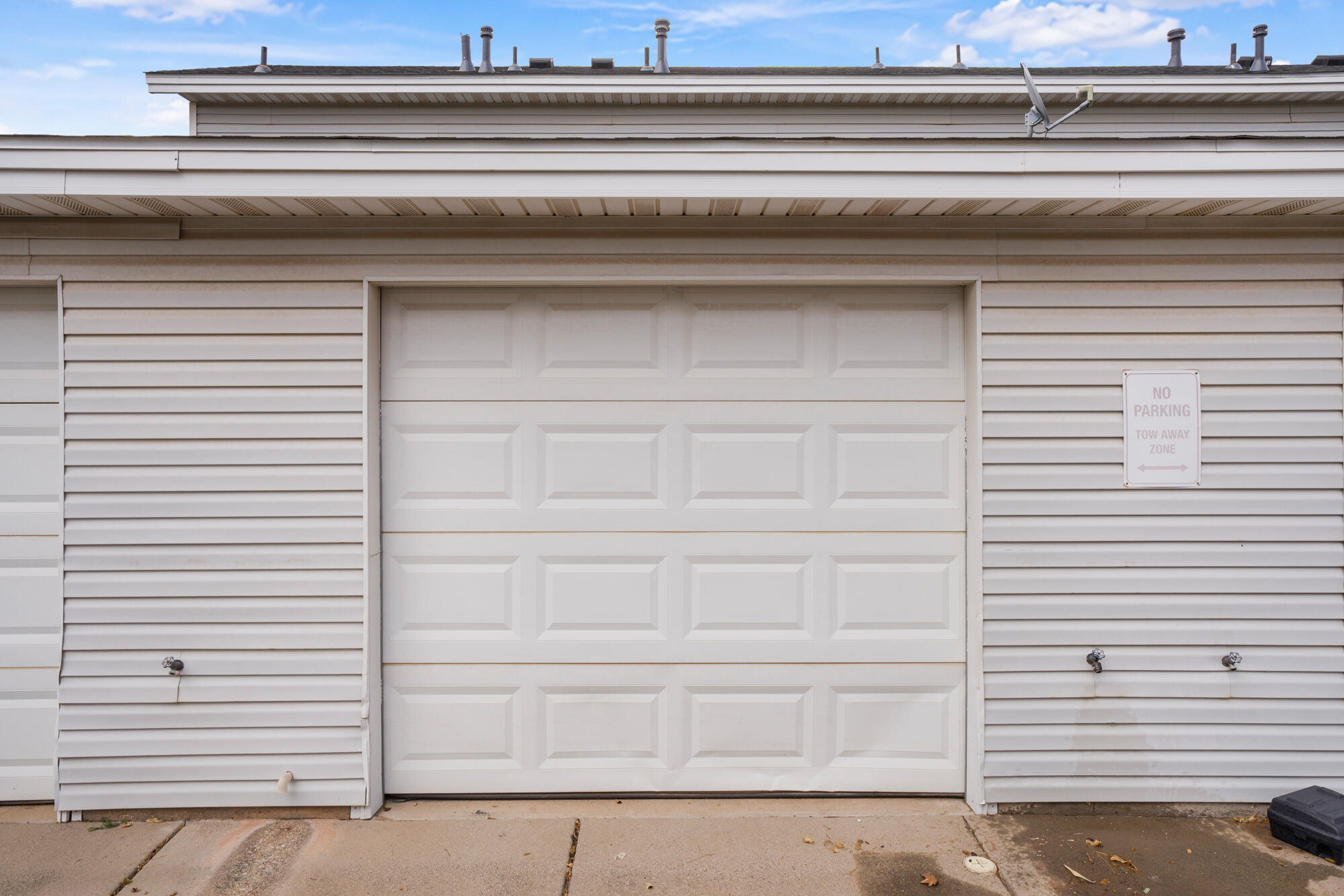 White paneled garage door beside a no-parking tow-away-zone sign.