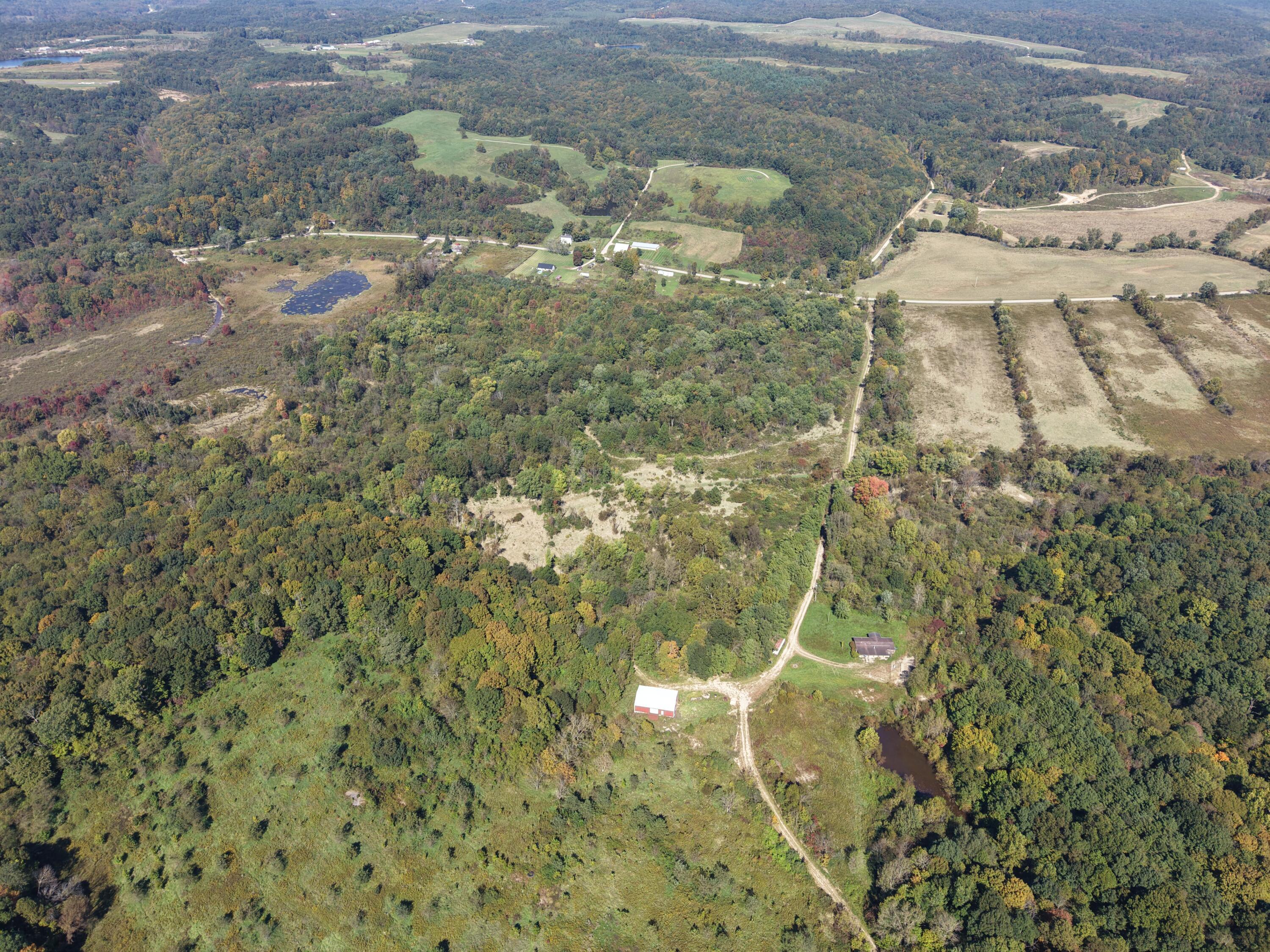Aerial view of wooded acreage with open fields, ponds, and outbuildings.