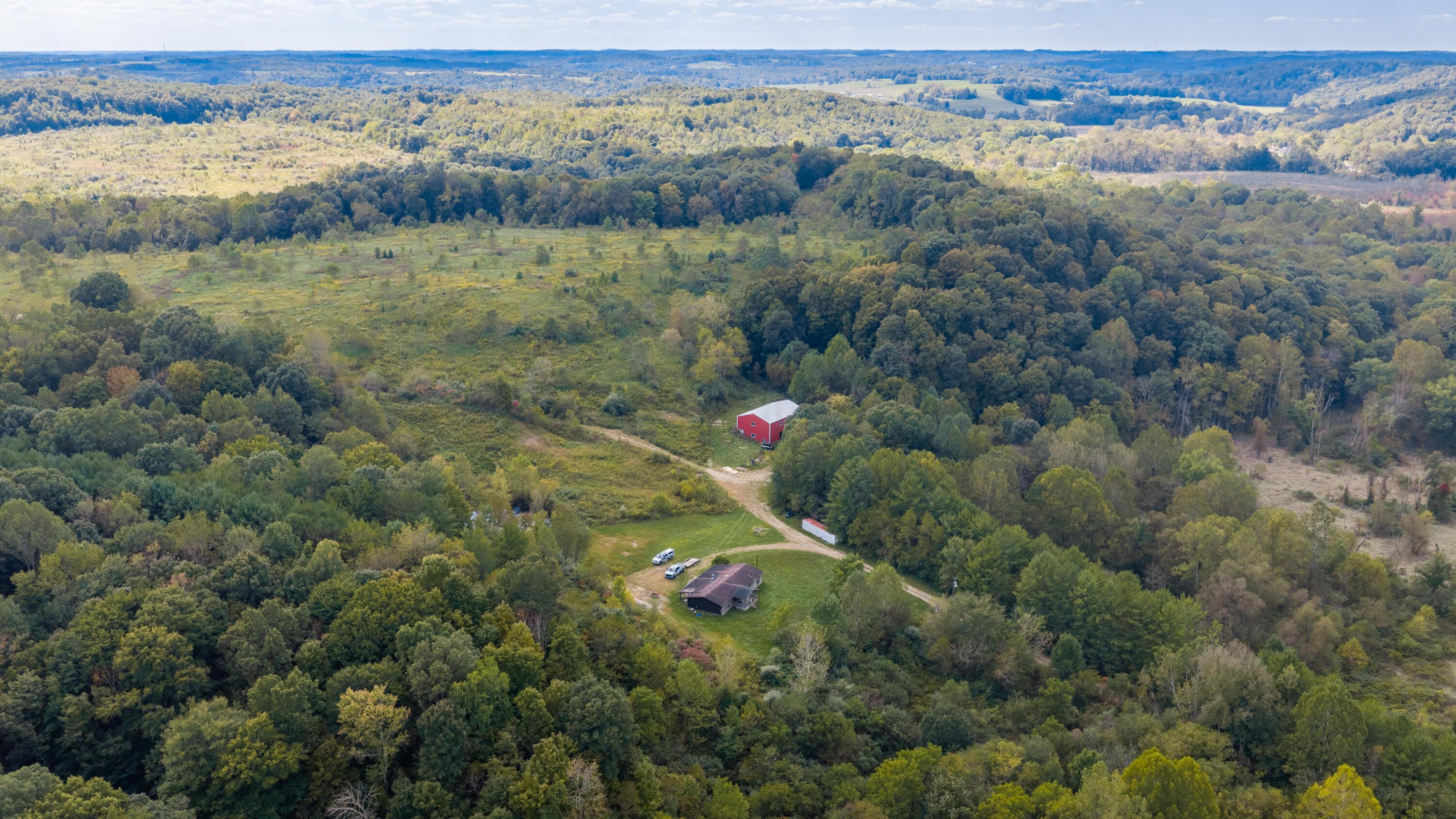 Aerial view of a wooded rural property with a home, red barn, and open clearing.