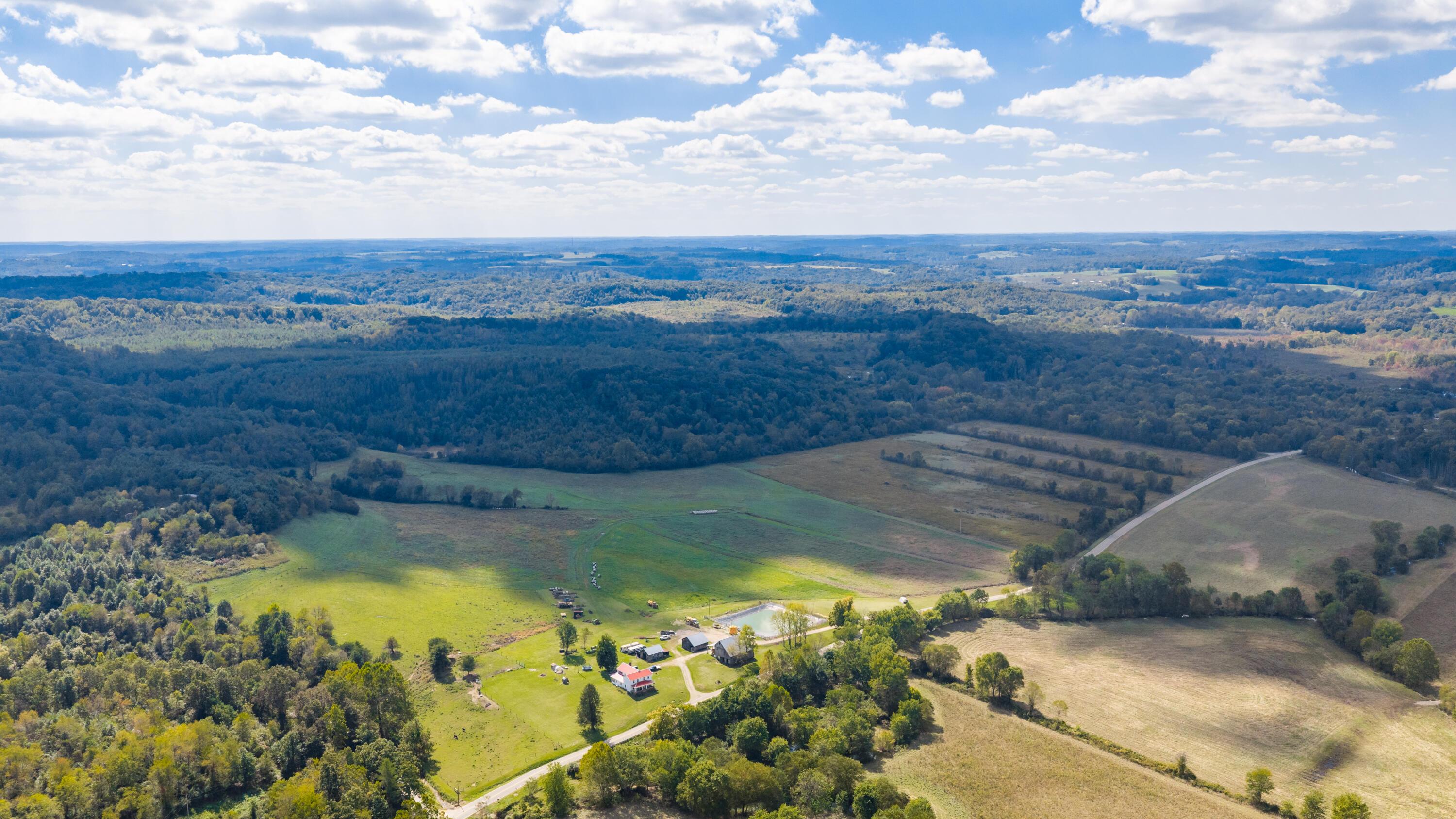 Aerial view of rural acreage with homes, open fields, winding roads, and surrounding woods.