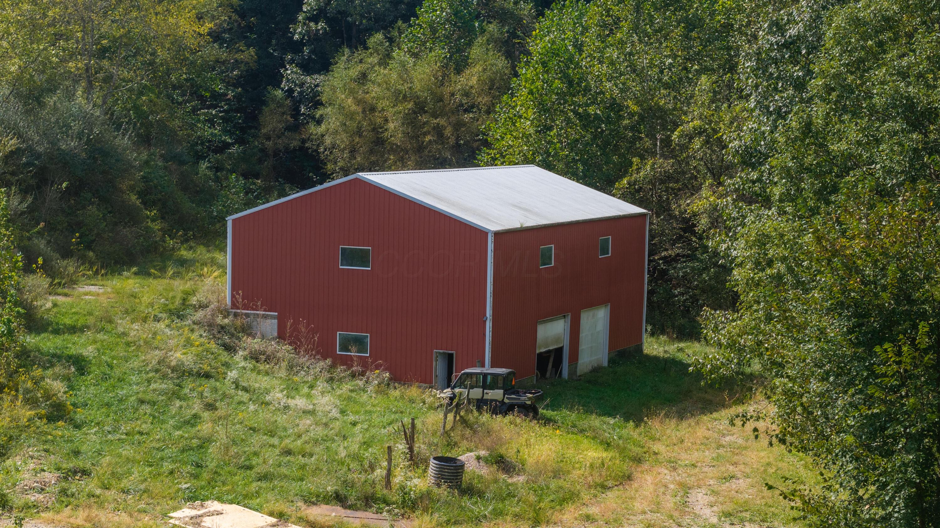 Red metal-sided barn in a grassy, wooded clearing, with a utility vehicle parked nearby.