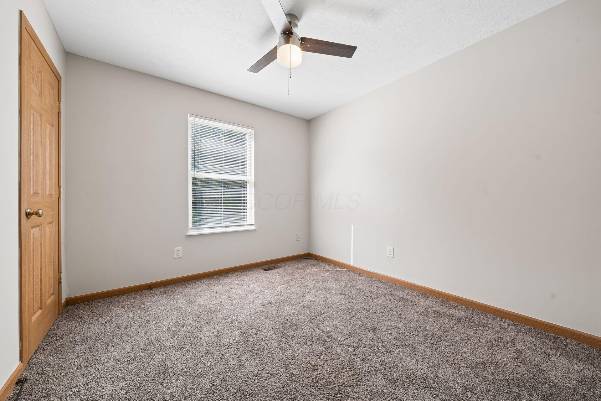 Vacant bedroom with gray carpet, a window with blinds, and a ceiling fan.