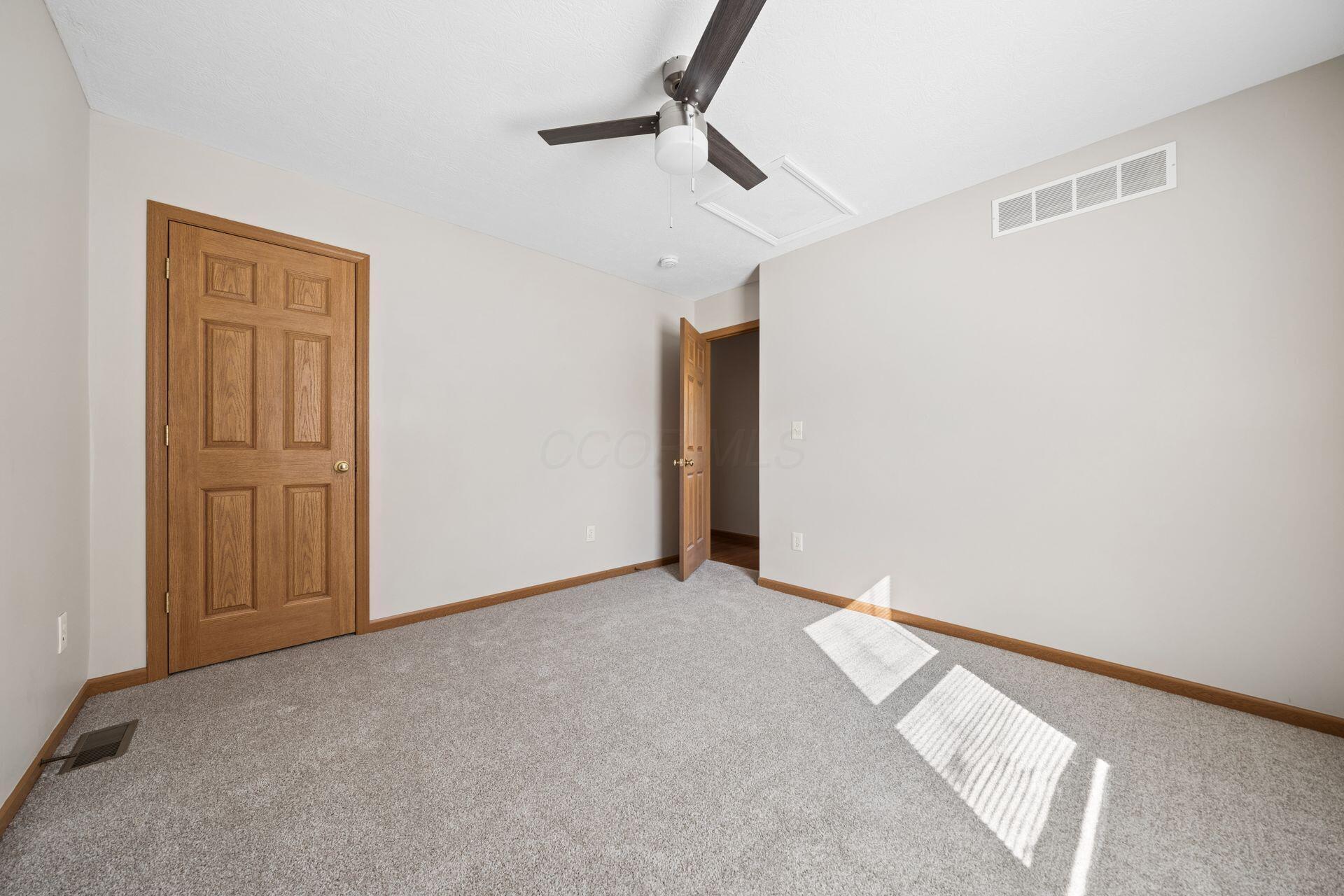 Empty carpeted bedroom with wooden doors and a ceiling fan.