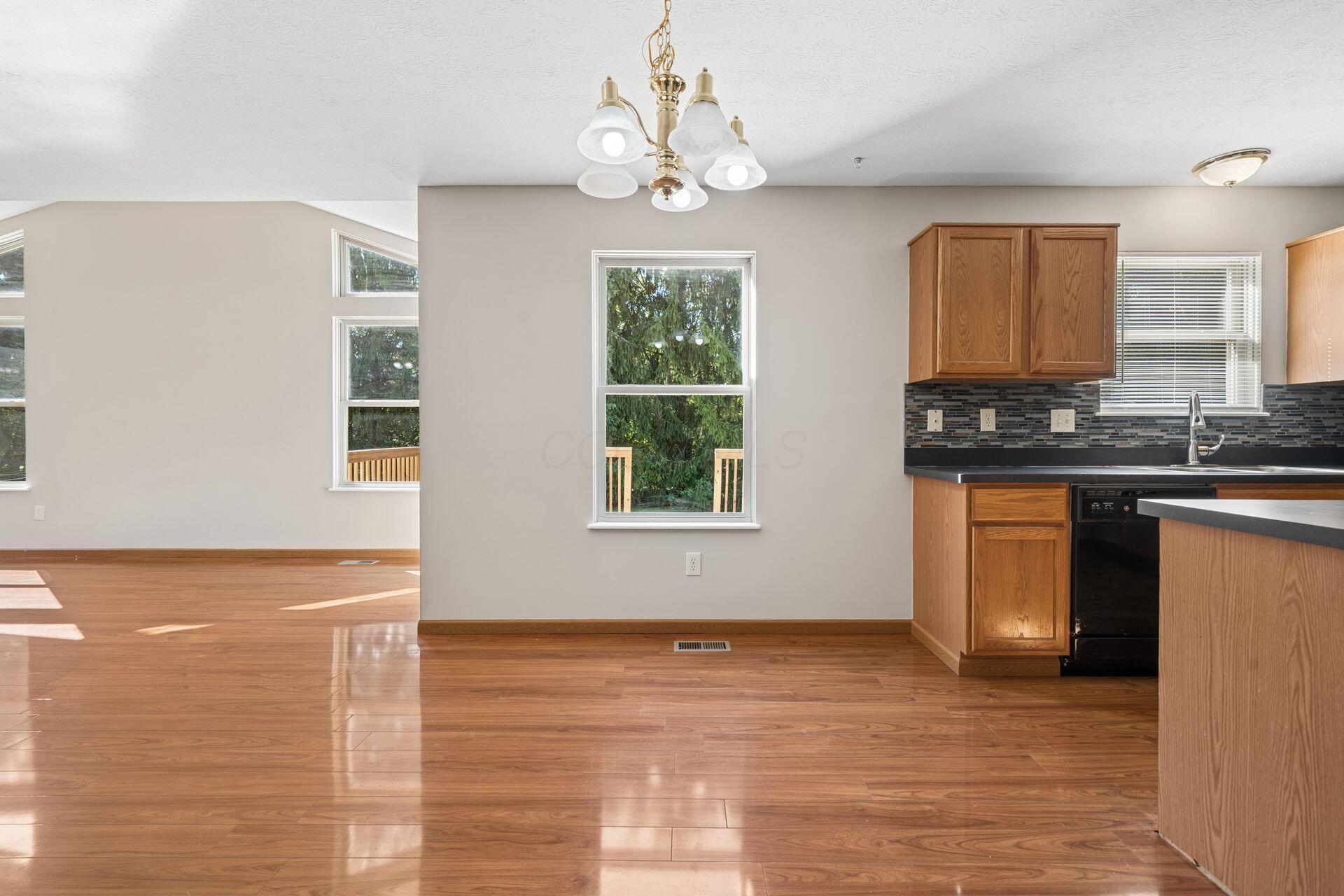 Vacant kitchen and dining area with hardwood floors, wood cabinets, and windows overlooking greenery.