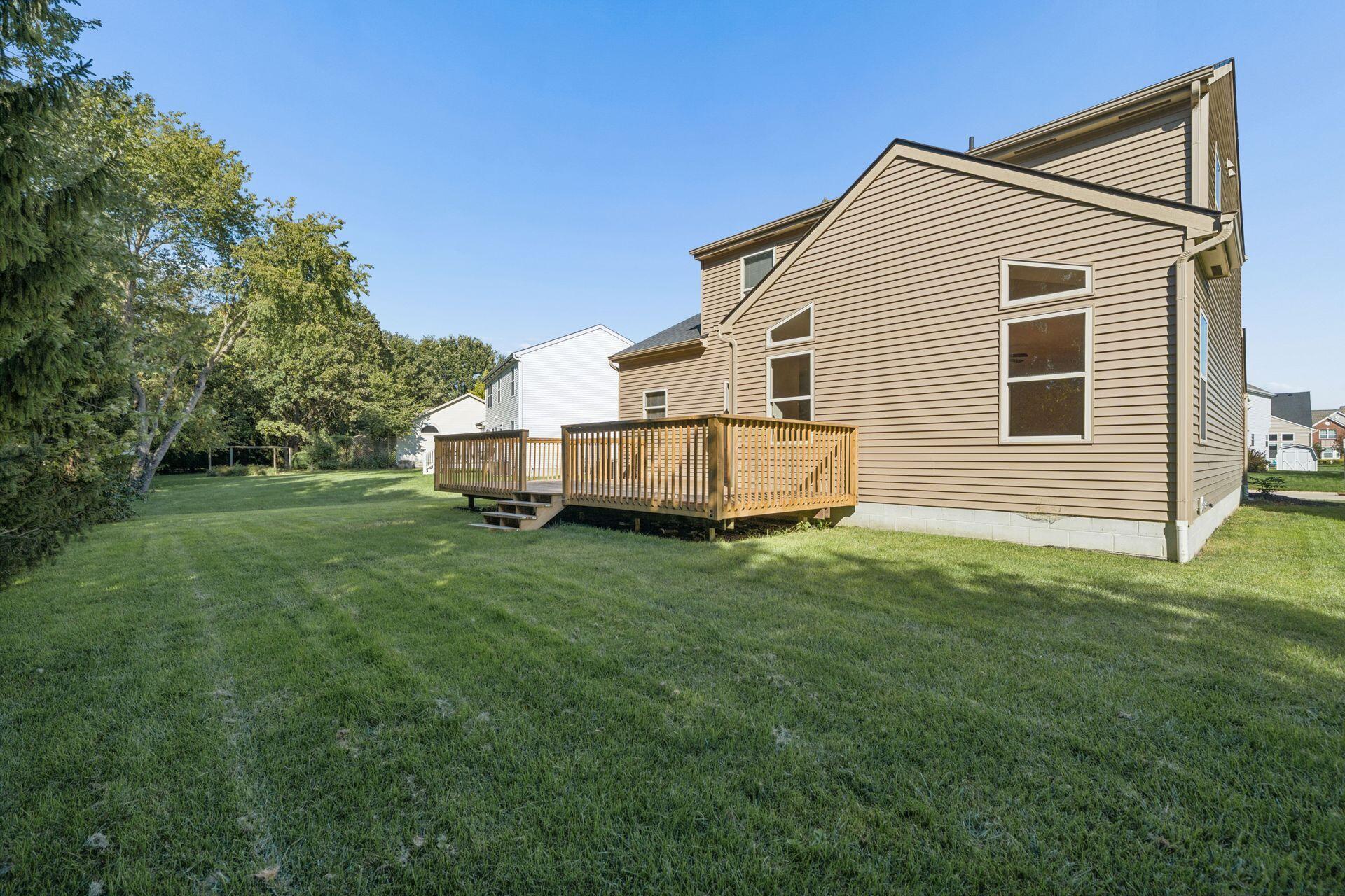 Rear of a tan two-story home with a raised wooden deck and spacious grassy backyard.
