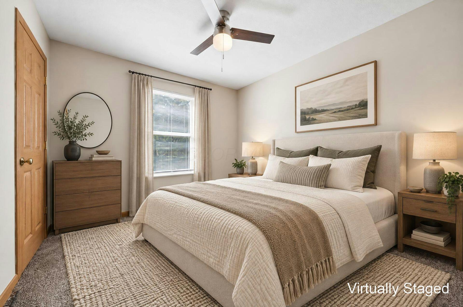 Staged bedroom with a cream bed, wood furnishings, curtained window, and ceiling fan.