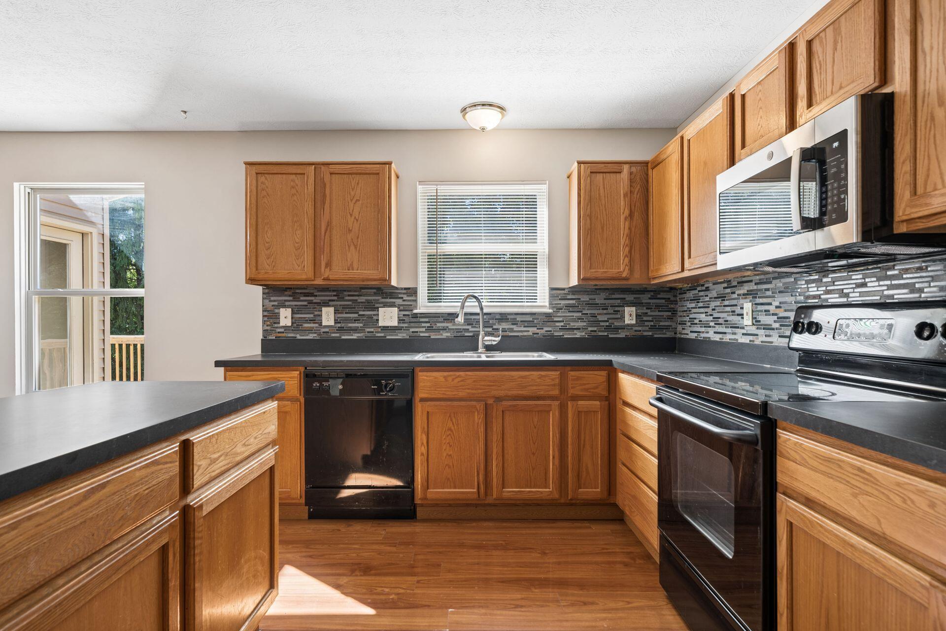 Kitchen with oak cabinets, a gray mosaic backsplash, and black and stainless steel appliances.