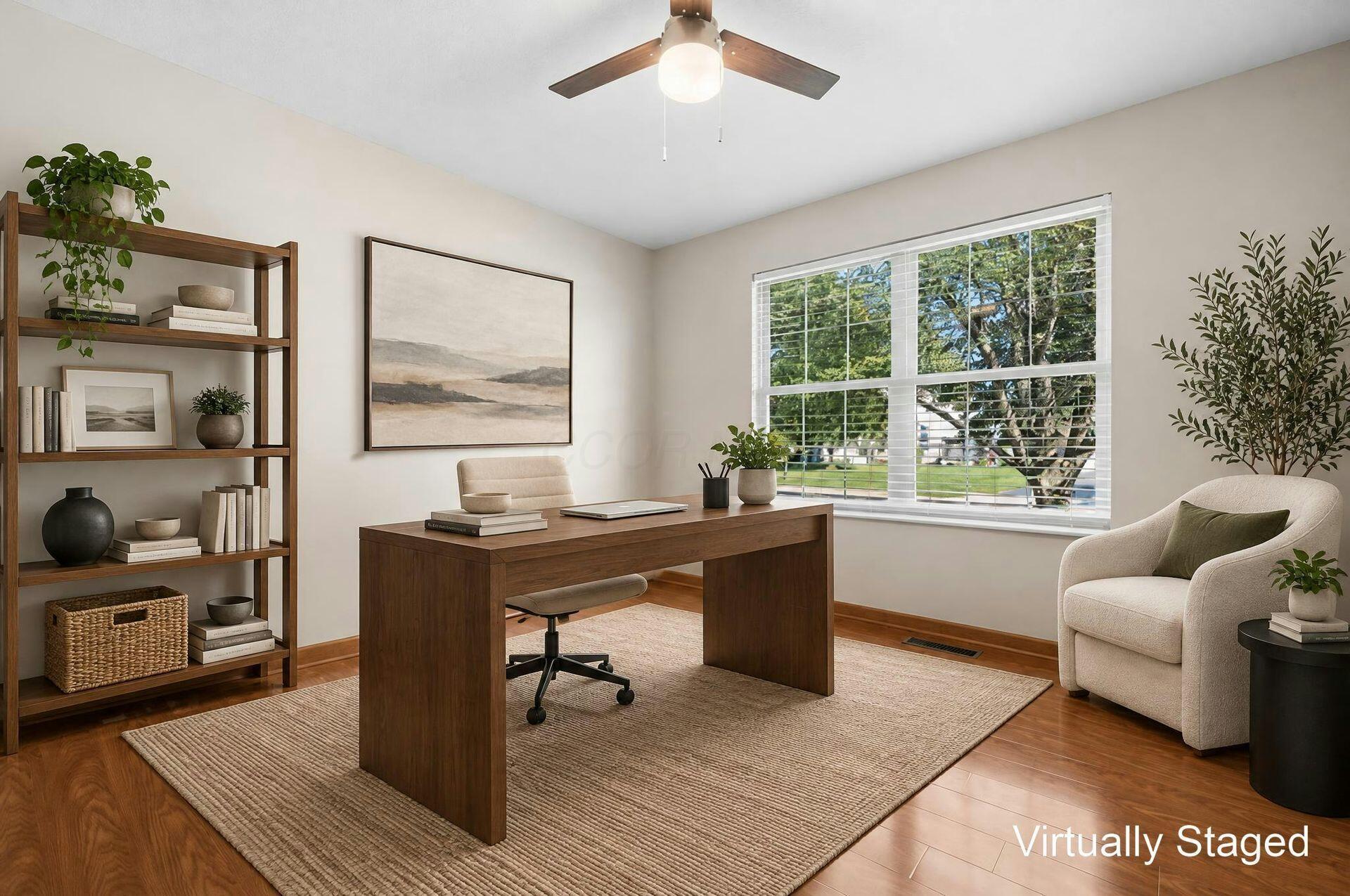 Virtually staged home office with a dark wood desk, bookcase, and large window.
