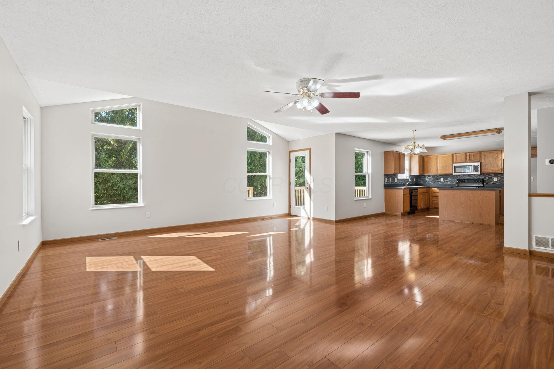 Open living area with vaulted ceiling, polished hardwood floors, and adjoining oak-cabinet kitchen.